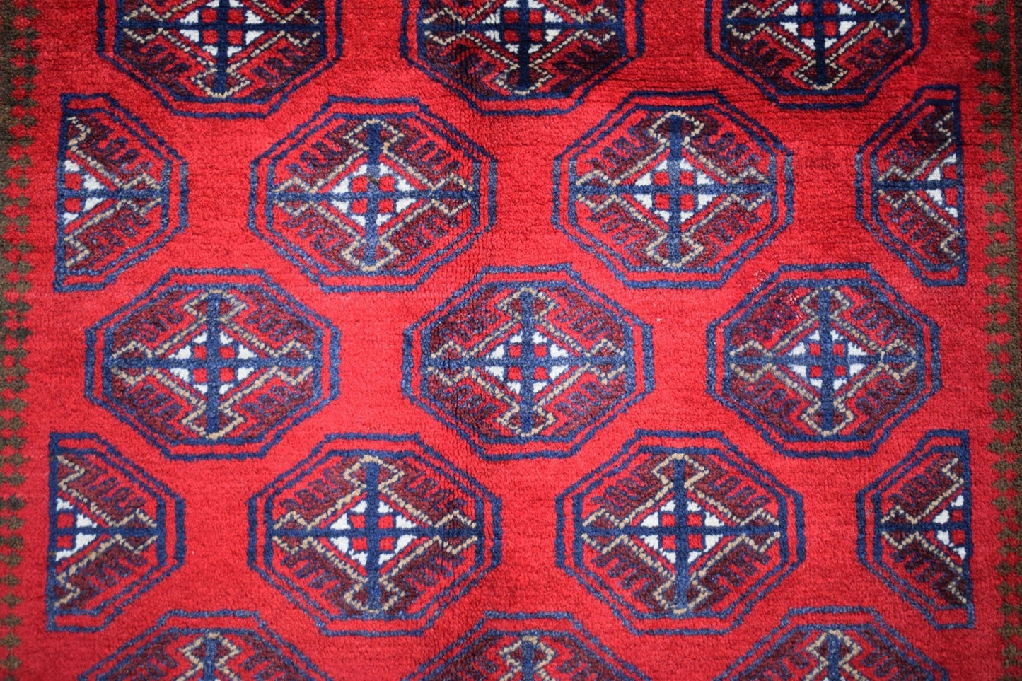 A vintage Afghan Baluch rug featuring a repeating geometric pattern in red, blue, and white.