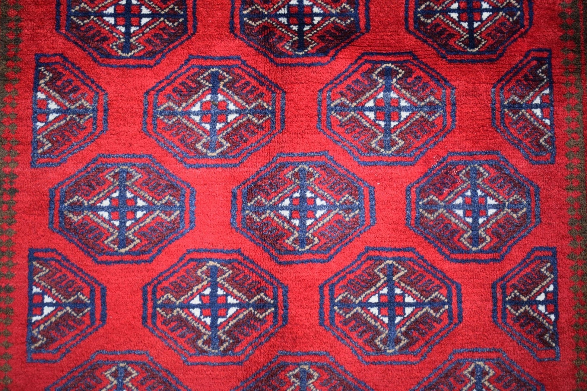 A vintage Afghan Baluch rug featuring a repeating geometric pattern in red, blue, and white.