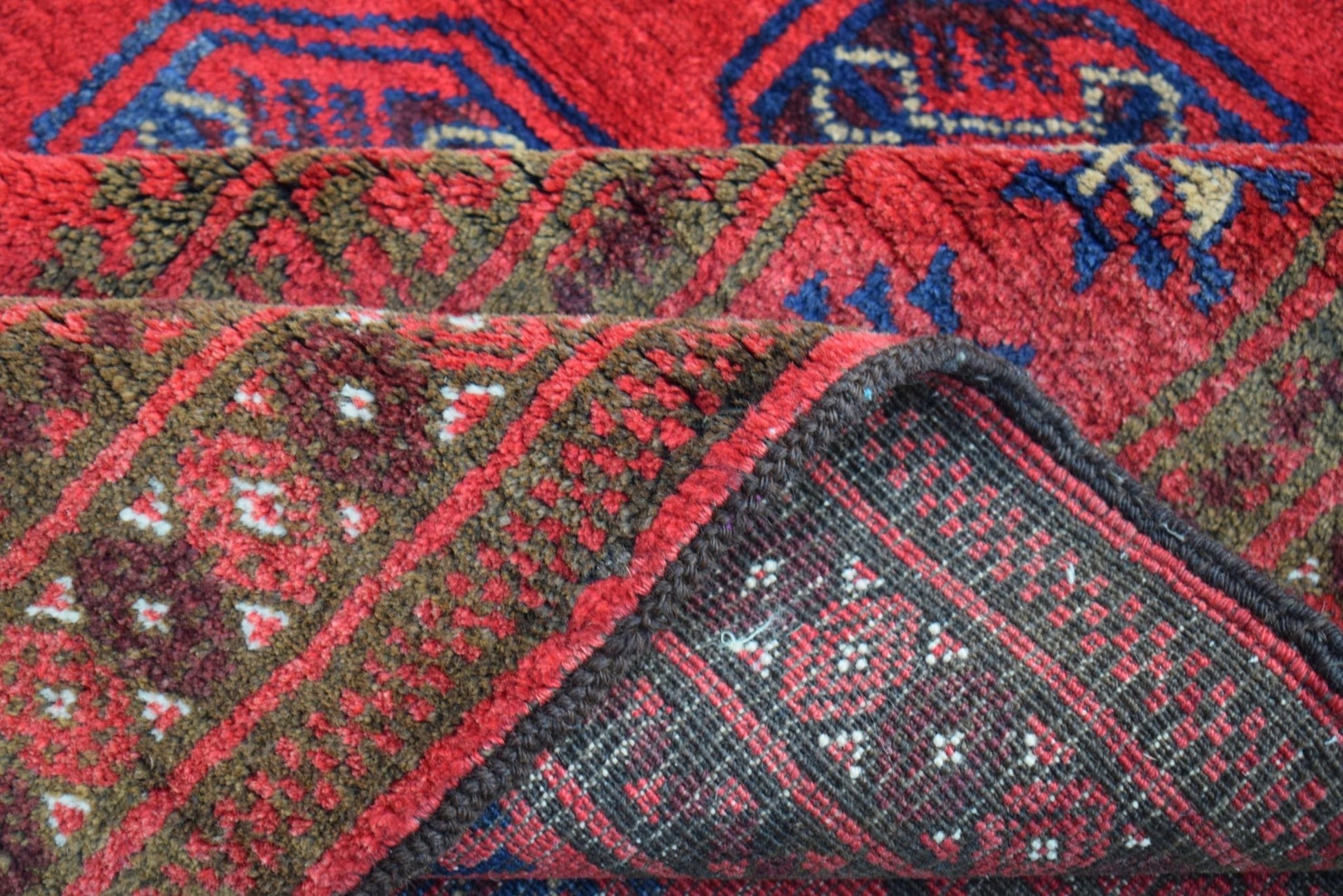A folded vintage Afghan Baluch rug featuring traditional red and blue geometric tribal patterns.