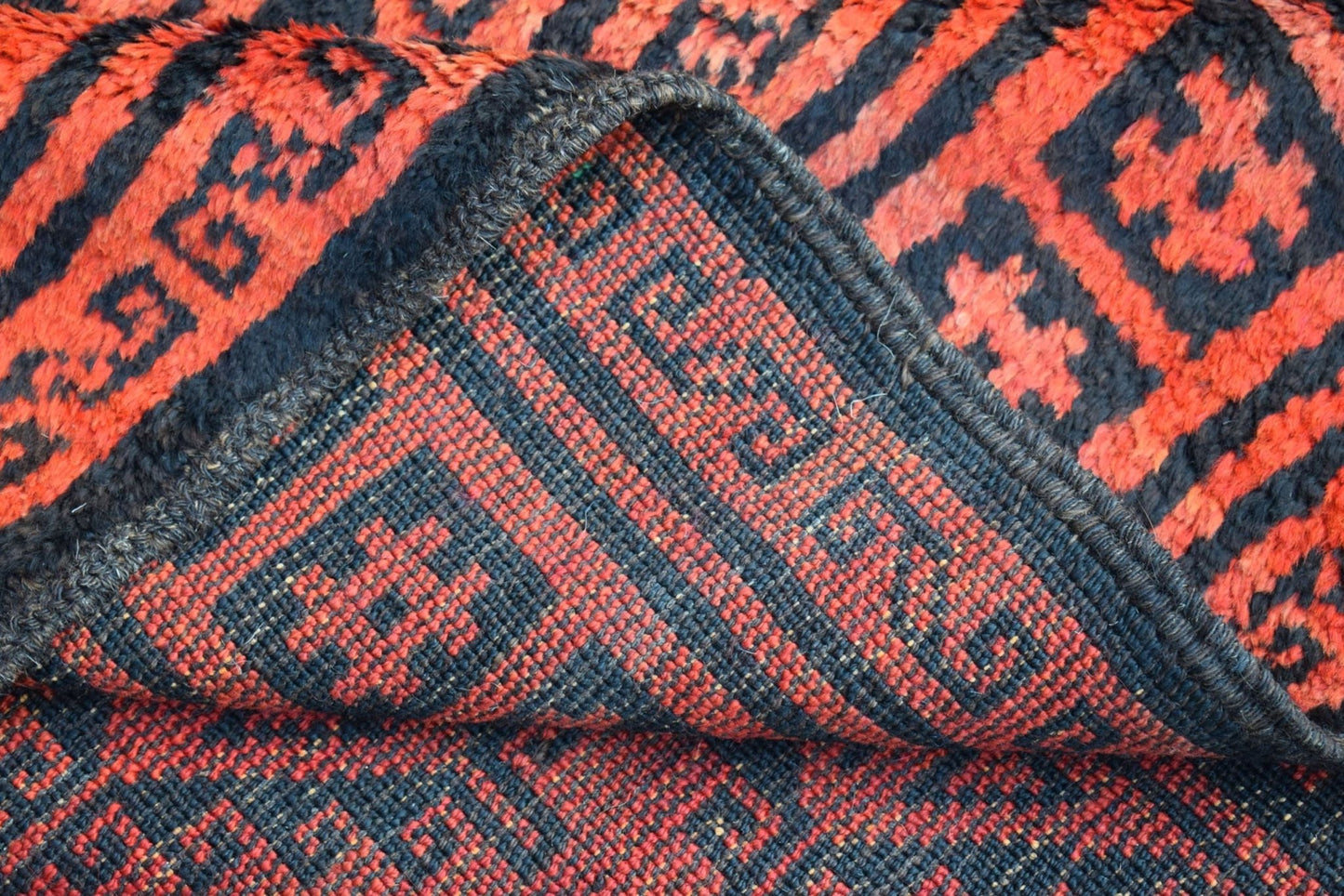 A close-up view of a vintage Afghan Baluch rug showing its red and black geometric wool weave.
