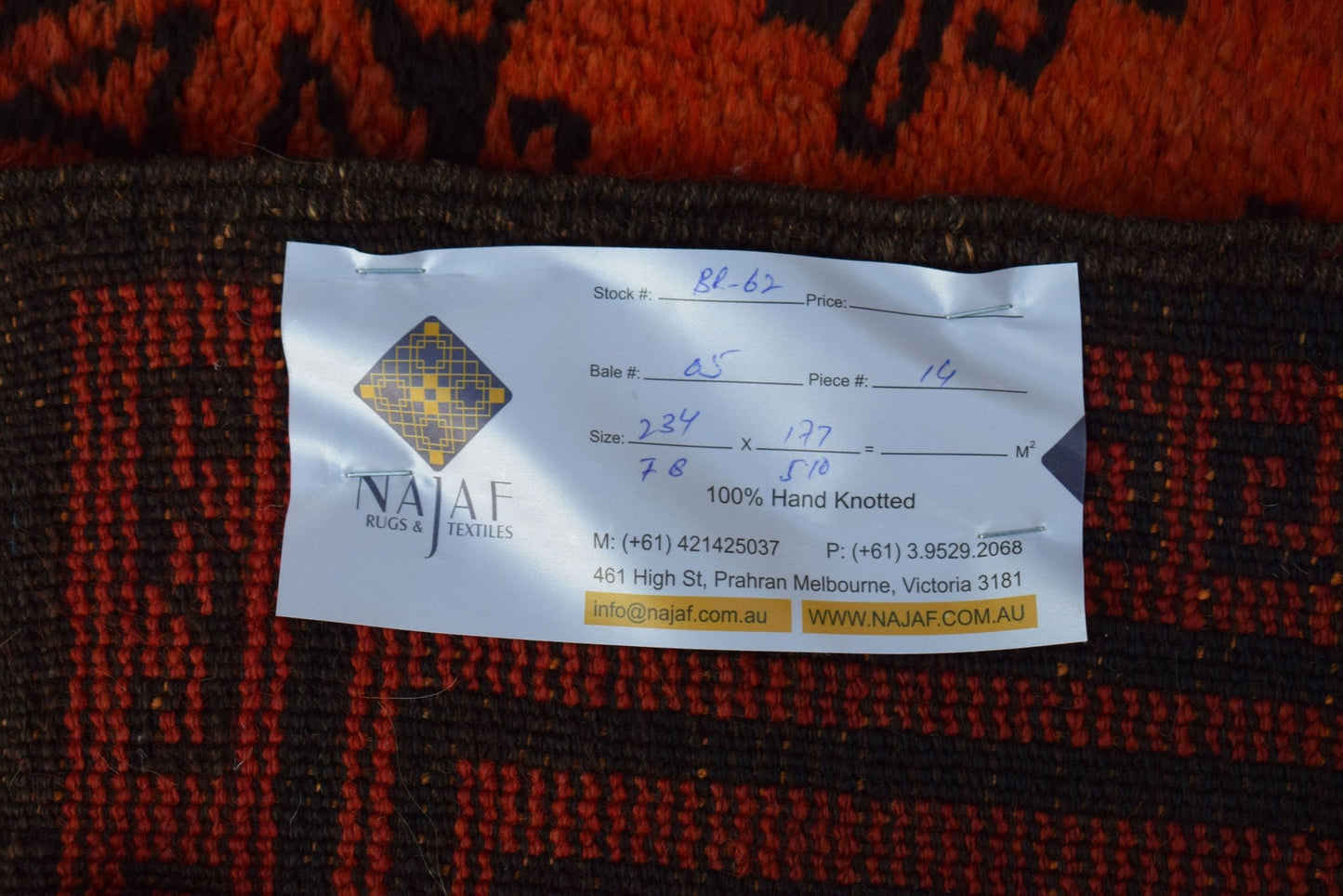 A vintage Afghan Baluch rug with a dark red and black geometric pattern and a product label.