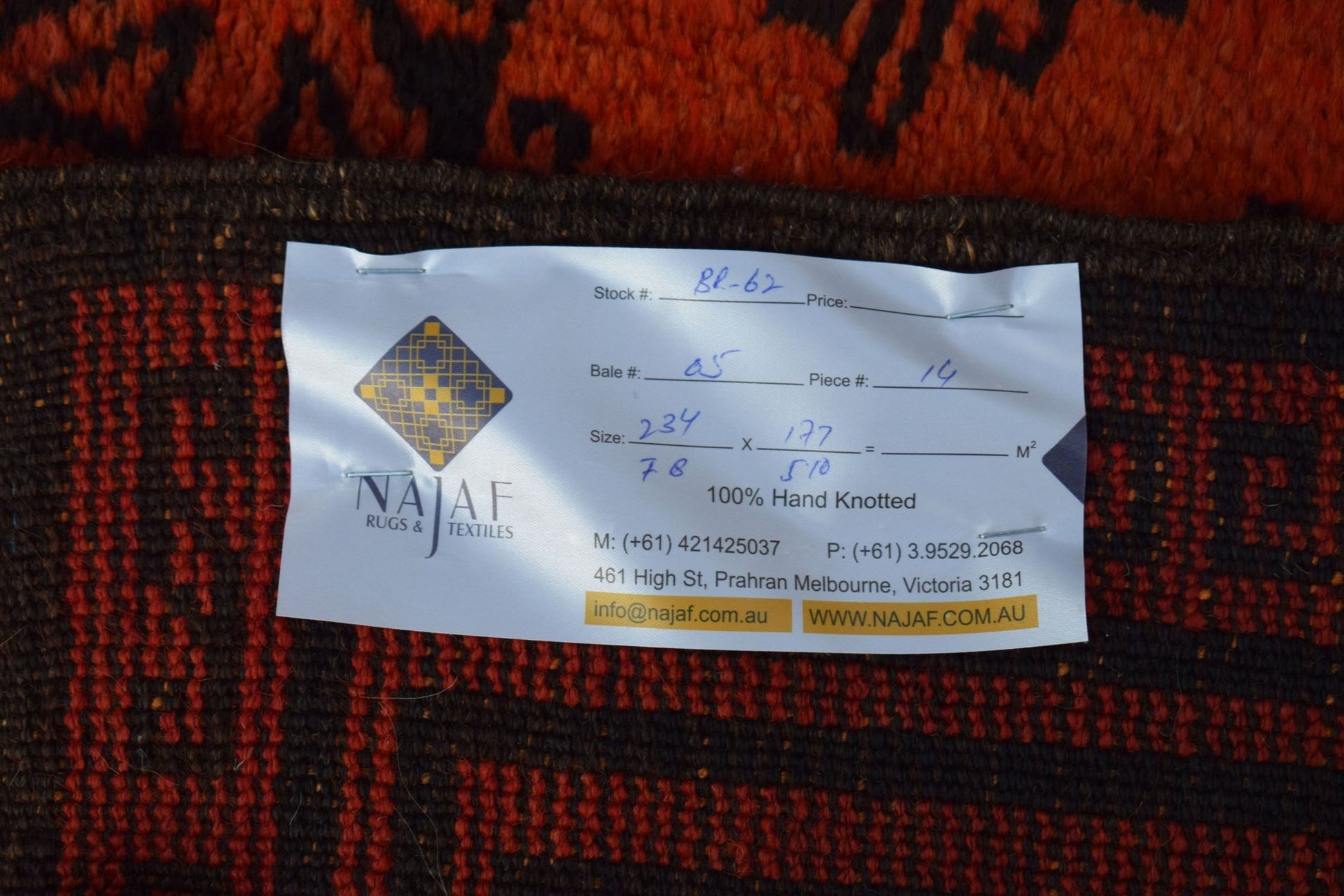 A vintage Afghan Baluch rug with a dark red and black geometric pattern and a product label.