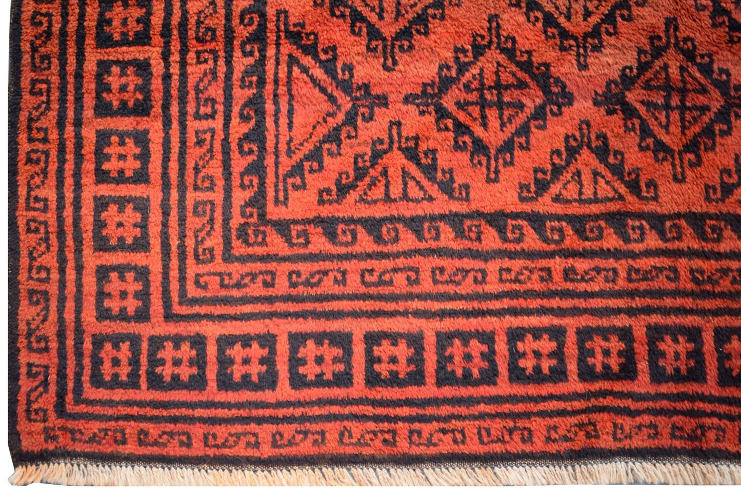 A vintage Afghan Baluch rug featuring a geometric black pattern on a deep red wool background.