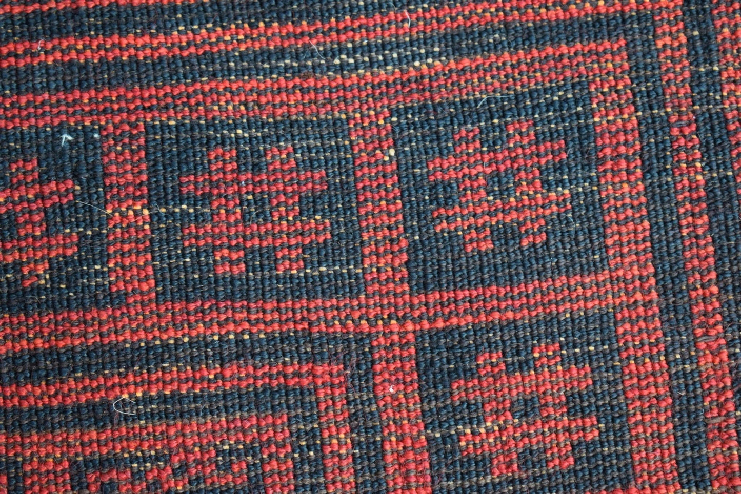 A close-up of a vintage Afghan Baluch wool rug featuring a geometric red and black pattern.