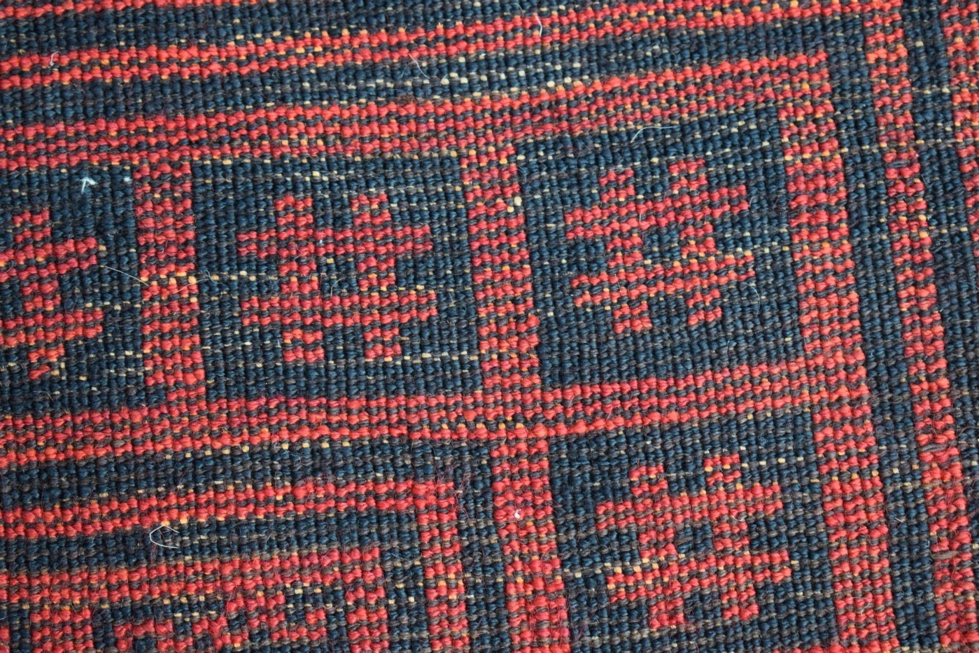 A close-up of a vintage Afghan Baluch wool rug featuring a geometric red and black pattern.