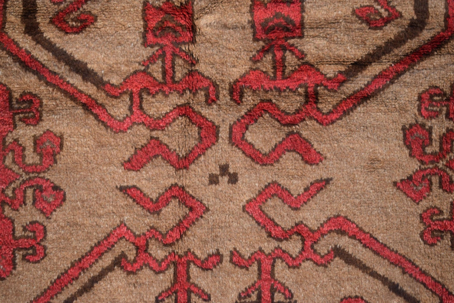 A close-up of a vintage Afghan Baluch wool rug featuring geometric red patterns on a brown field.
