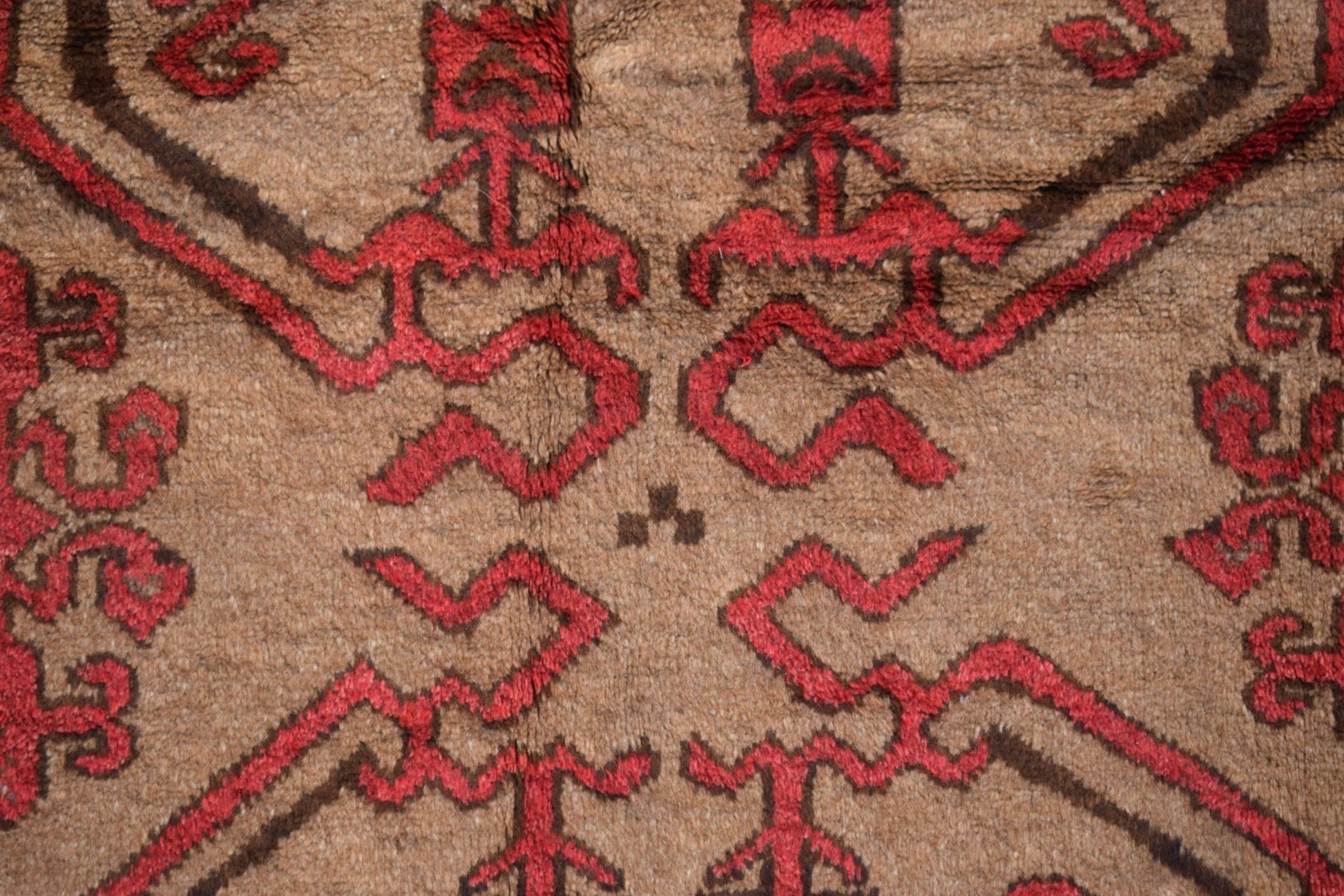 A close-up of a vintage Afghan Baluch wool rug featuring geometric red patterns on a brown field.