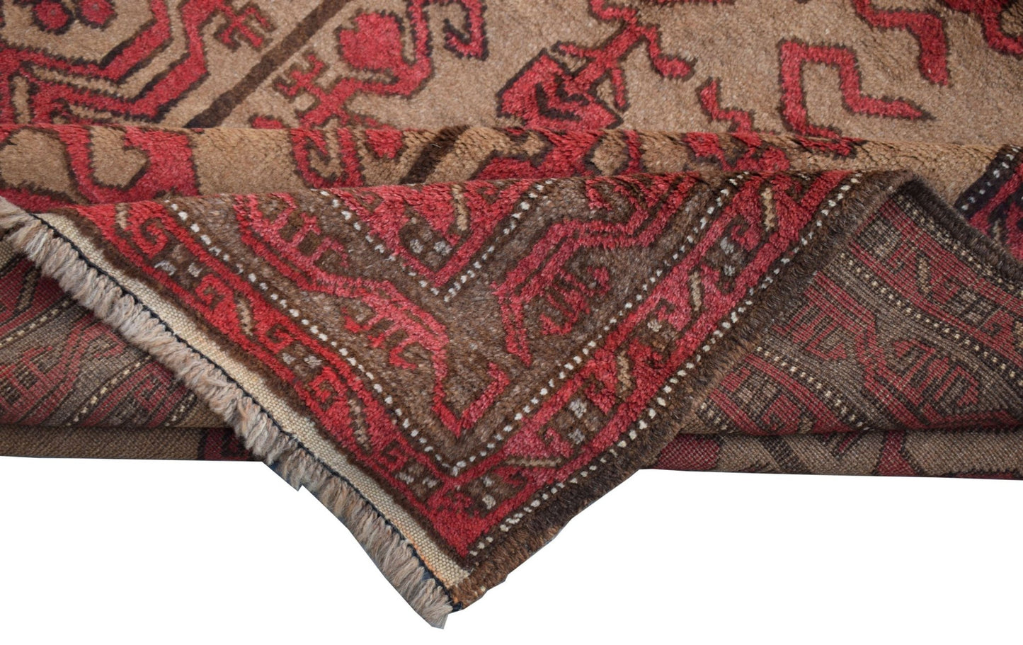 A vintage Afghan Baluch rug with a folded corner showing its red and brown geometric pattern.