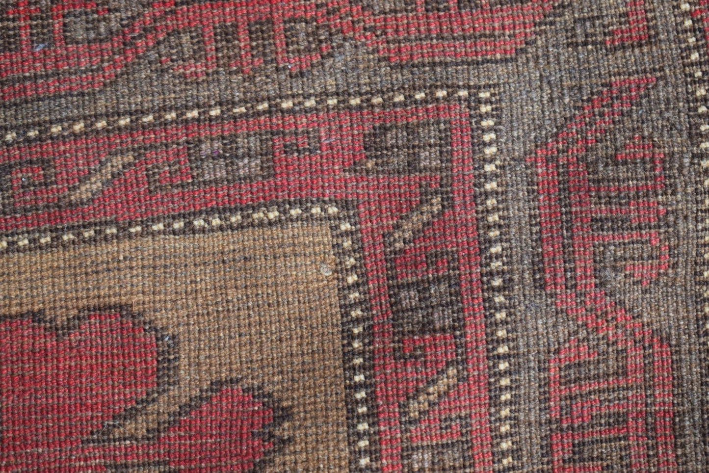 A close-up of a vintage Afghan Baluch rug featuring geometric patterns in red and brown wool.