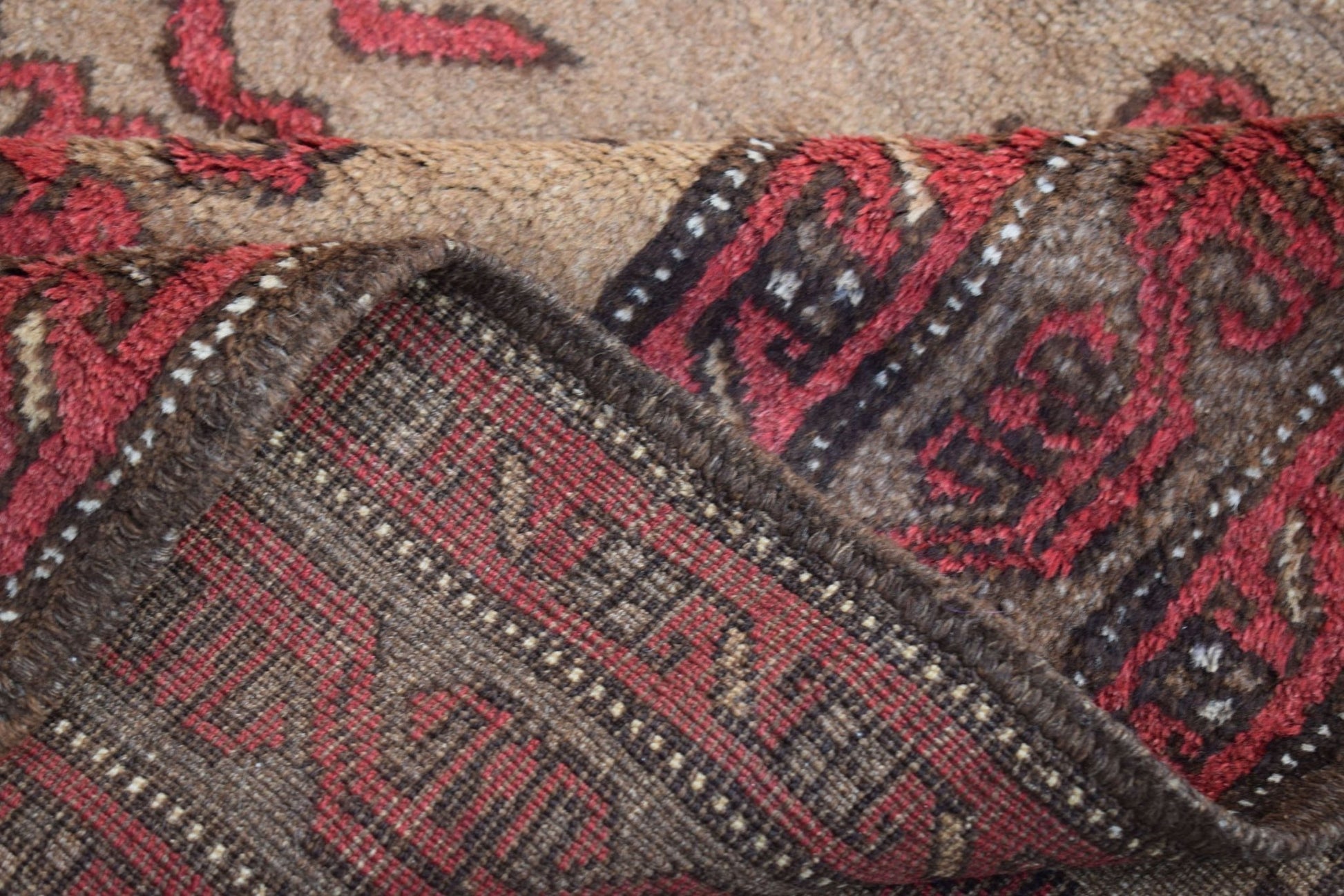 A folded vintage Afghan Baluch wool rug featuring a red and brown geometric tribal pattern.