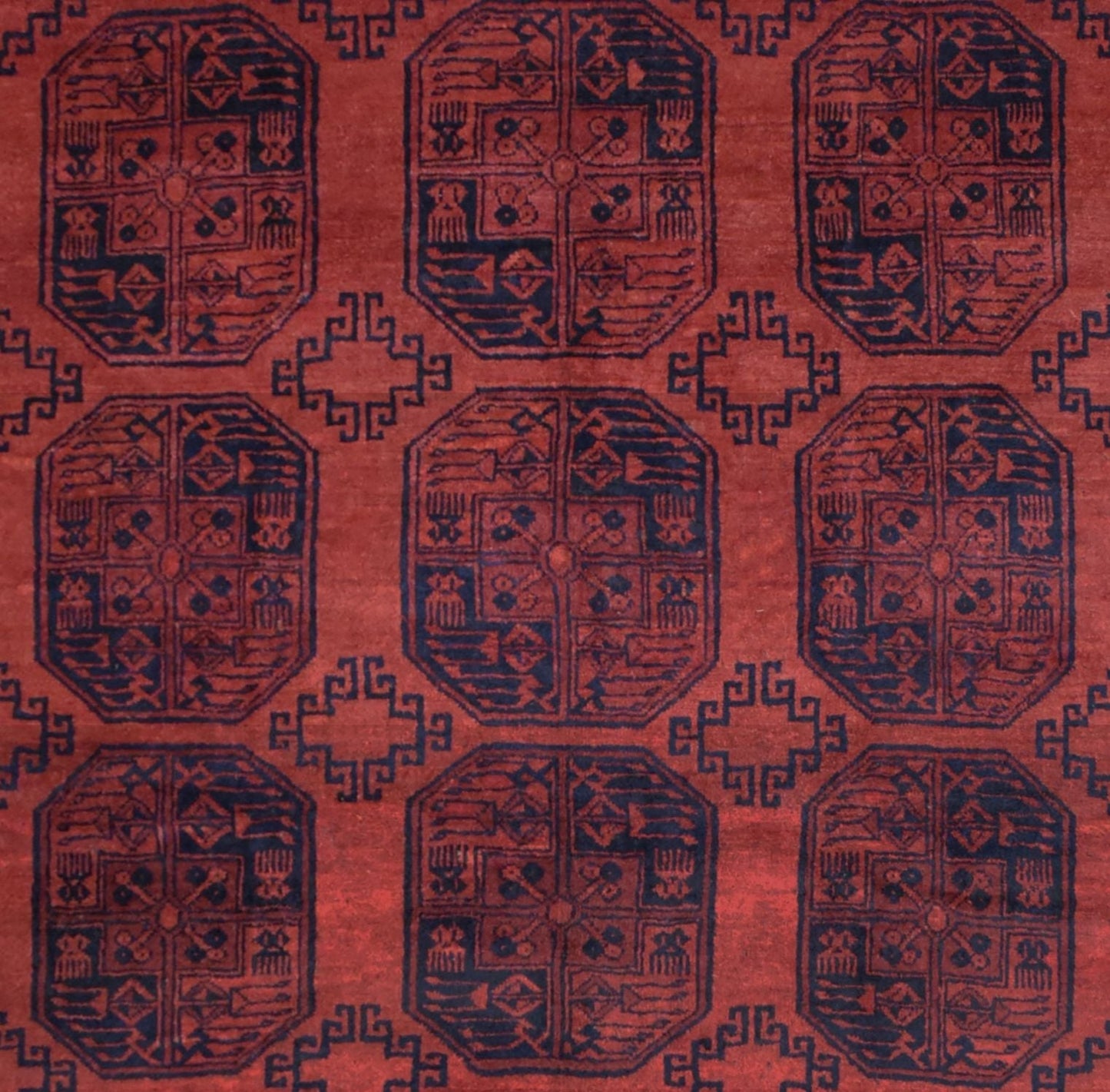 A vintage handmade Afghan Turkmen rug featuring a repeating geometric pattern in deep red and navy.