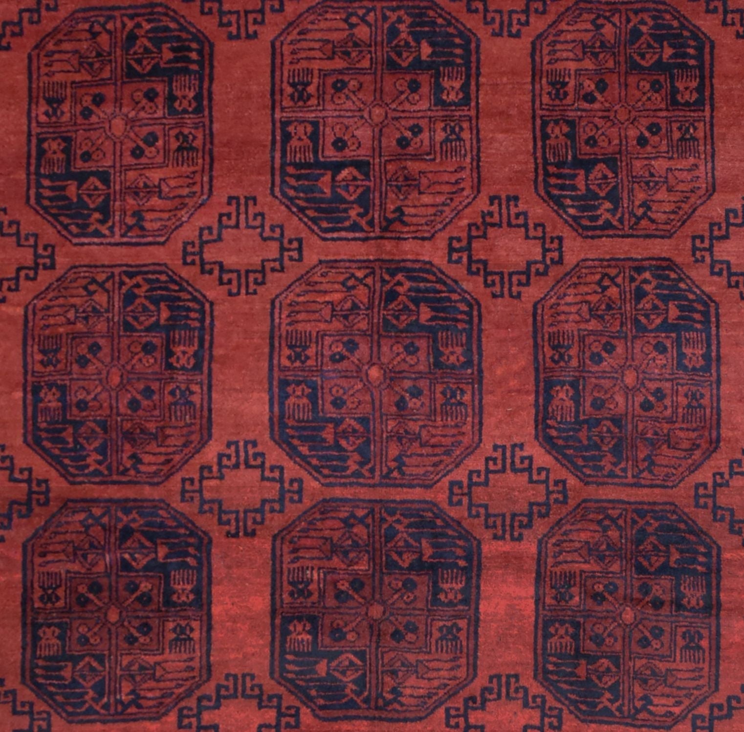 A vintage handmade Afghan Turkmen rug featuring a repeating geometric pattern in deep red and navy.