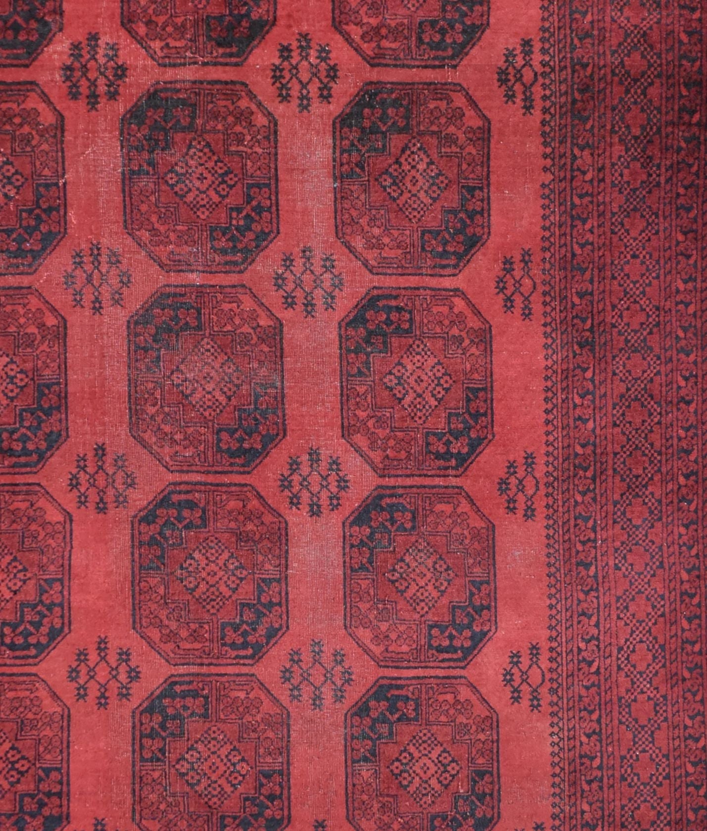 A vintage handmade Afghan Turkmen rug featuring repeating dark octagonal motifs on a red field.