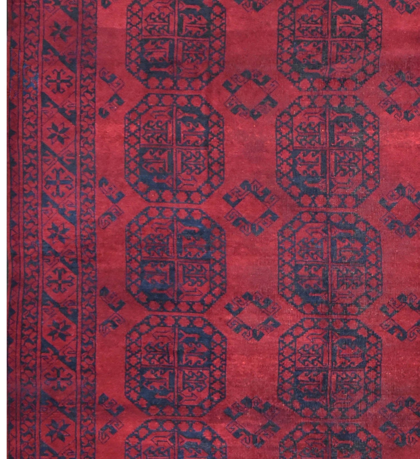 A vintage handmade Afghan Turkmen rug featuring repeating dark blue octagonal motifs on a red field.