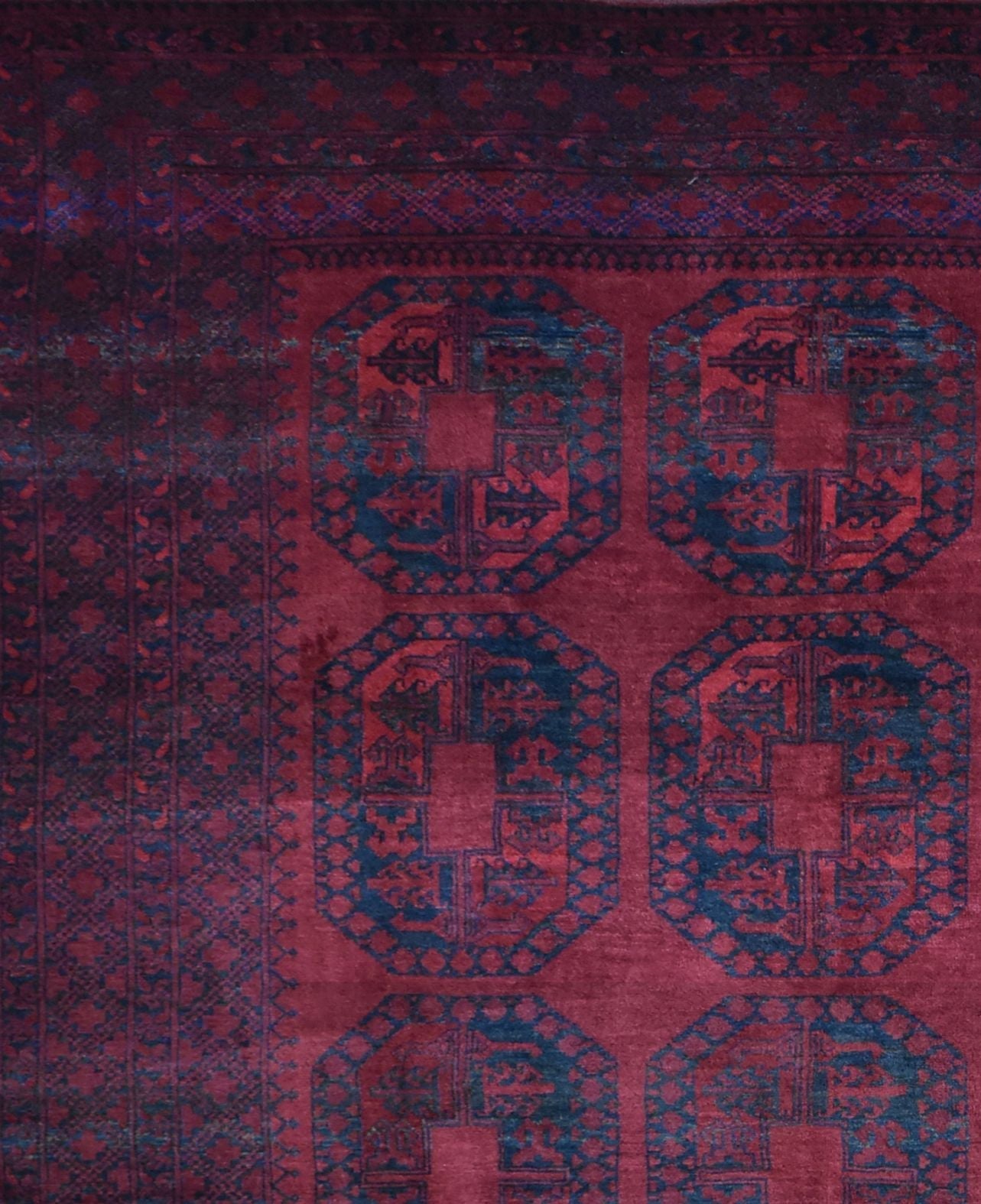 A vintage Afghan Turkmen rug featuring repeating dark blue geometric octagons on a deep red field.