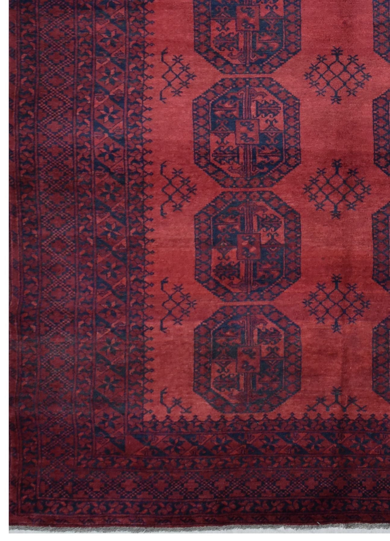 A vintage handmade Afghan Turkmen rug featuring dark blue geometric motifs on a red wool field.