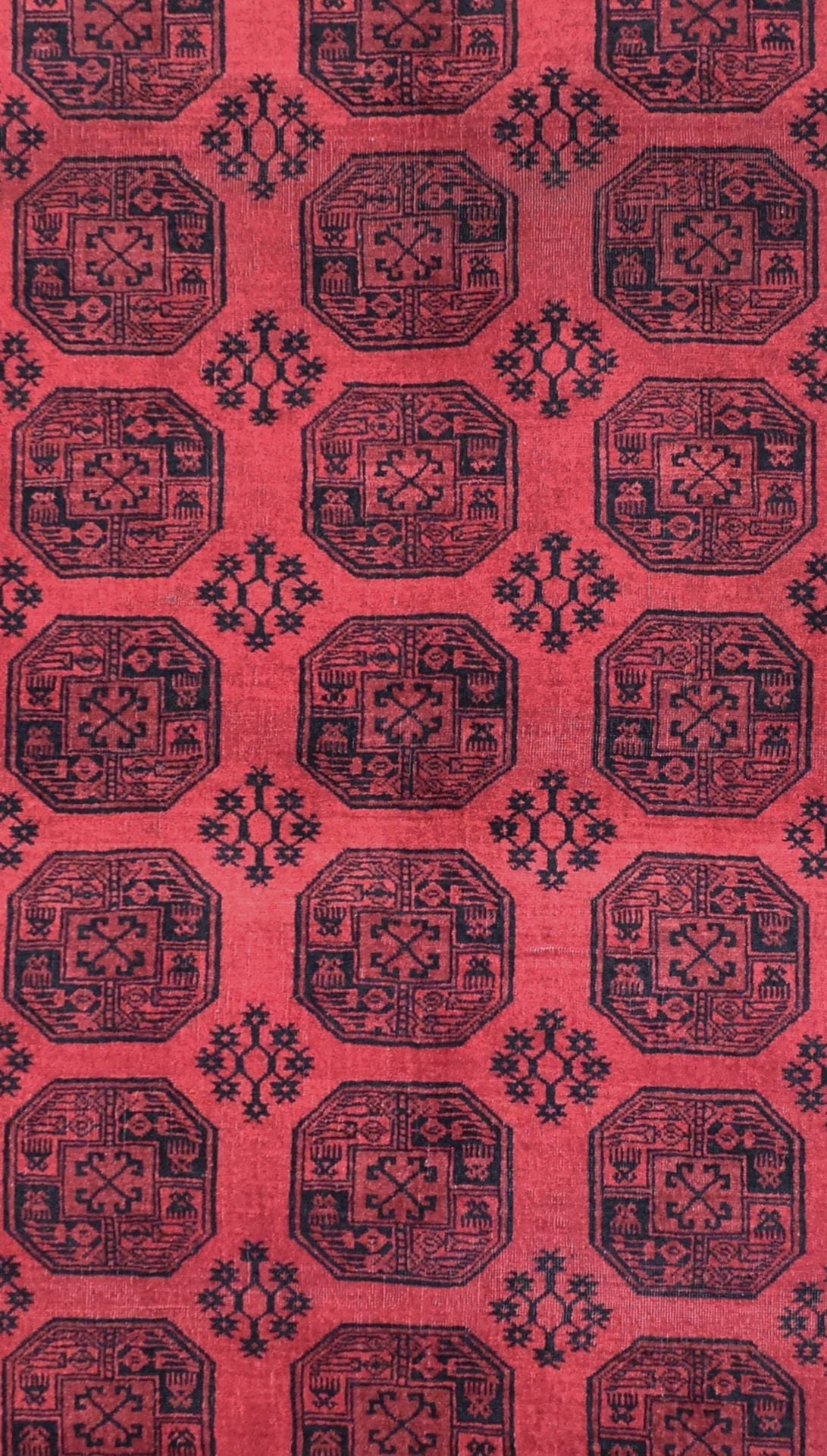 A vintage Afghan Turkmen rug featuring a repeating geometric octagonal pattern in black on red.