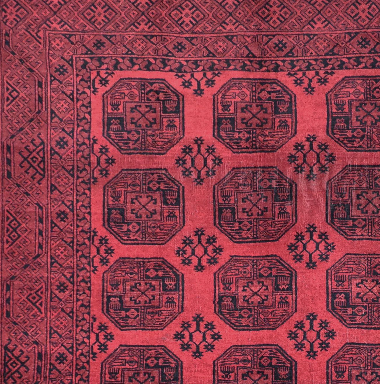 A vintage handmade Afghan Turkmen rug featuring repeating black octagonal motifs on a red field.
