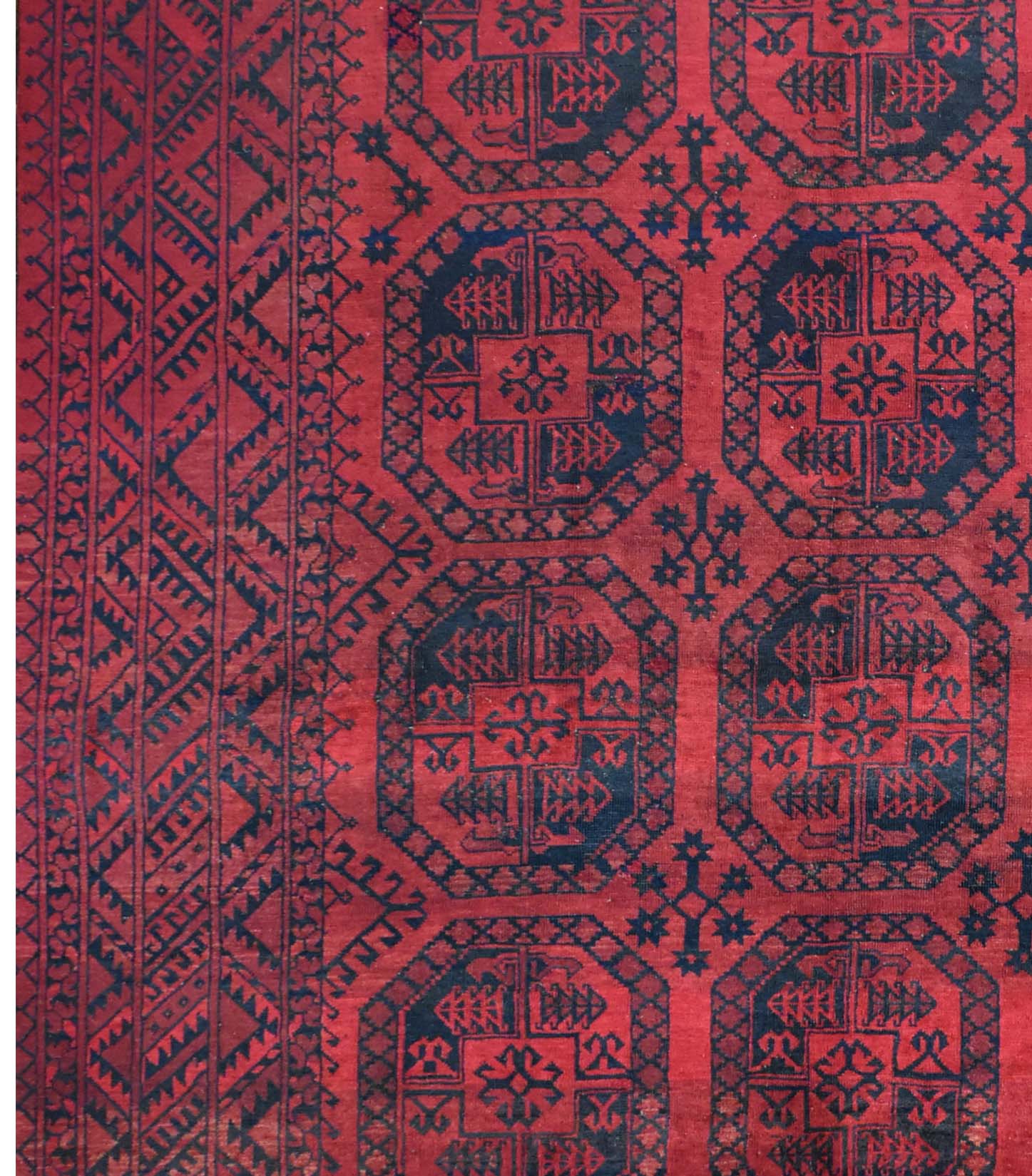 A vintage handmade Afghan Turkmen rug featuring repeating dark geometric octagons on a red field.