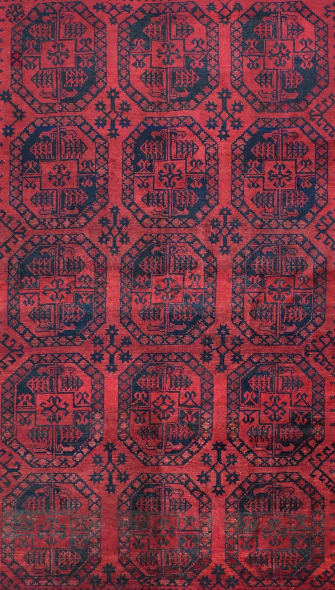 A vintage Afghan Turkmen rug featuring a repeating geometric gul pattern in red and dark blue.