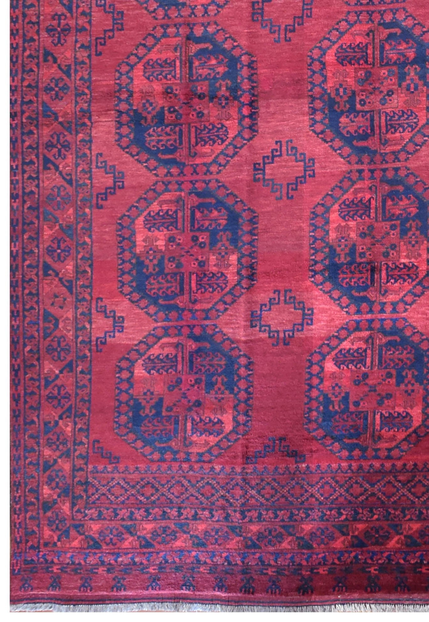 A vintage Afghan Turkmen rug featuring repeating dark blue octagonal guls on a deep red field.