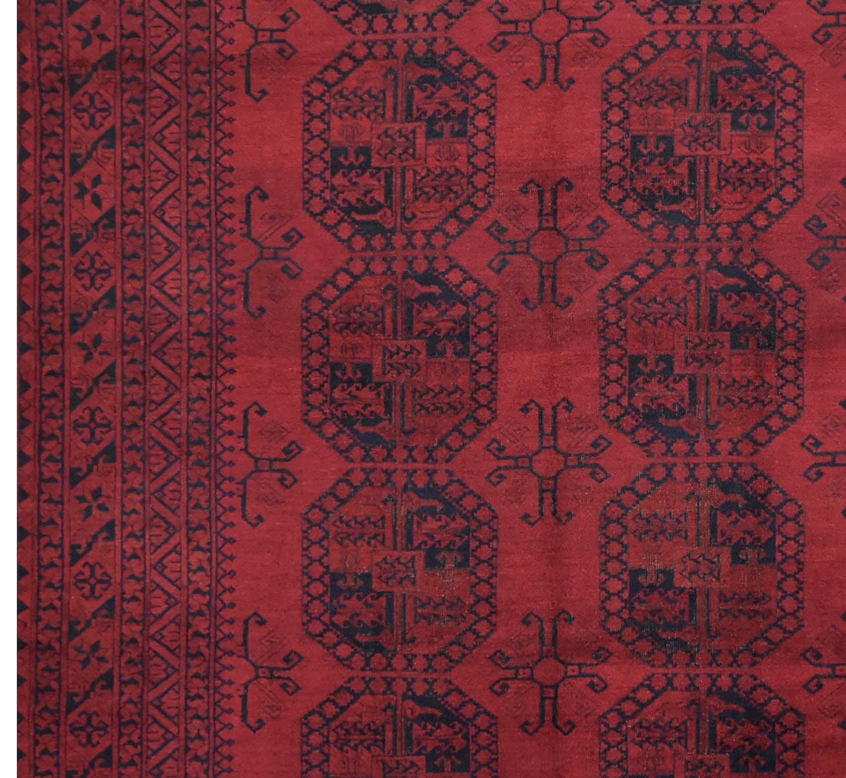 A vintage Afghan Turkmen rug featuring repeating dark geometric octagons on a deep red background.