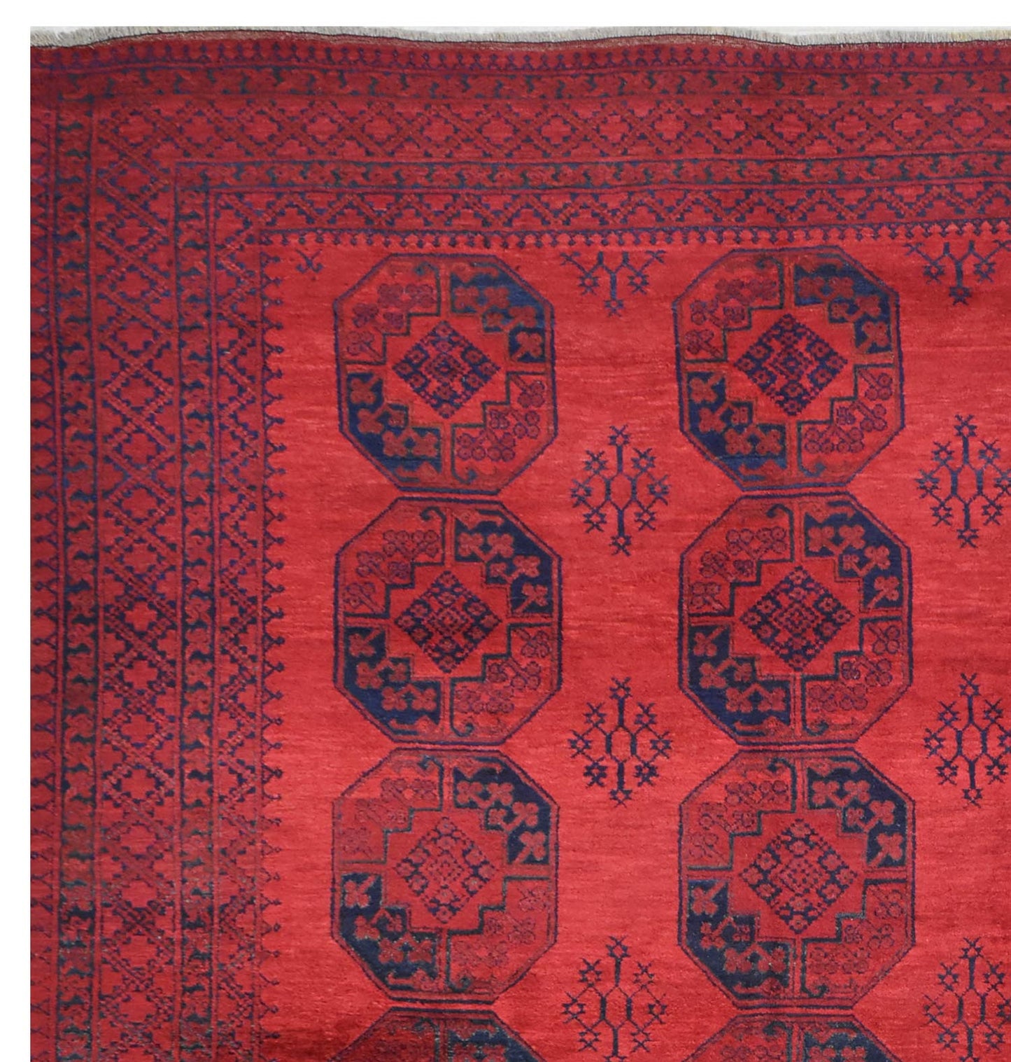 A vintage Afghan Turkmen rug featuring a red field with repeating dark blue geometric octagons.