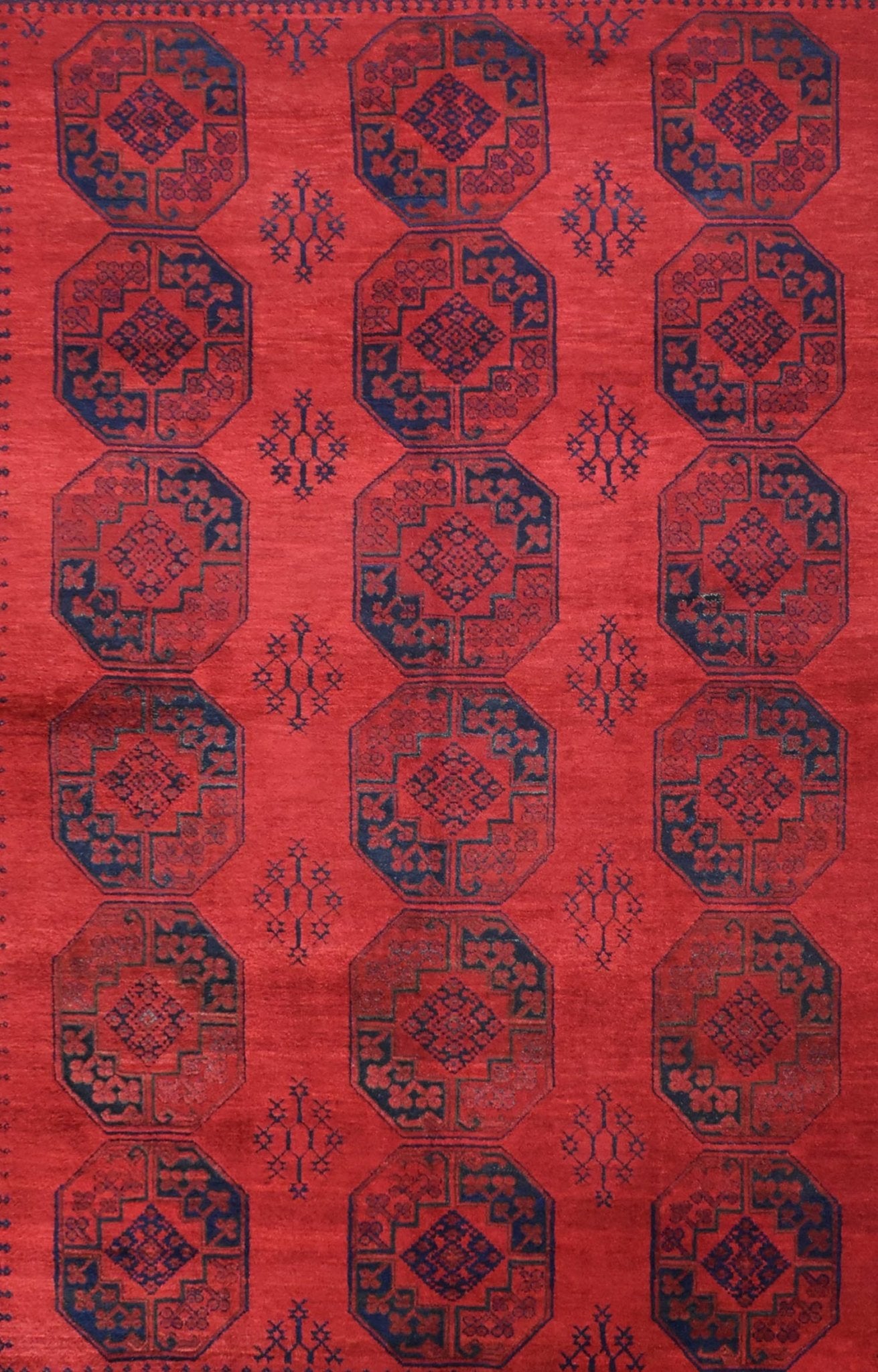A vintage handmade Afghan Turkmen rug featuring repeating dark blue octagonal motifs on a red field.