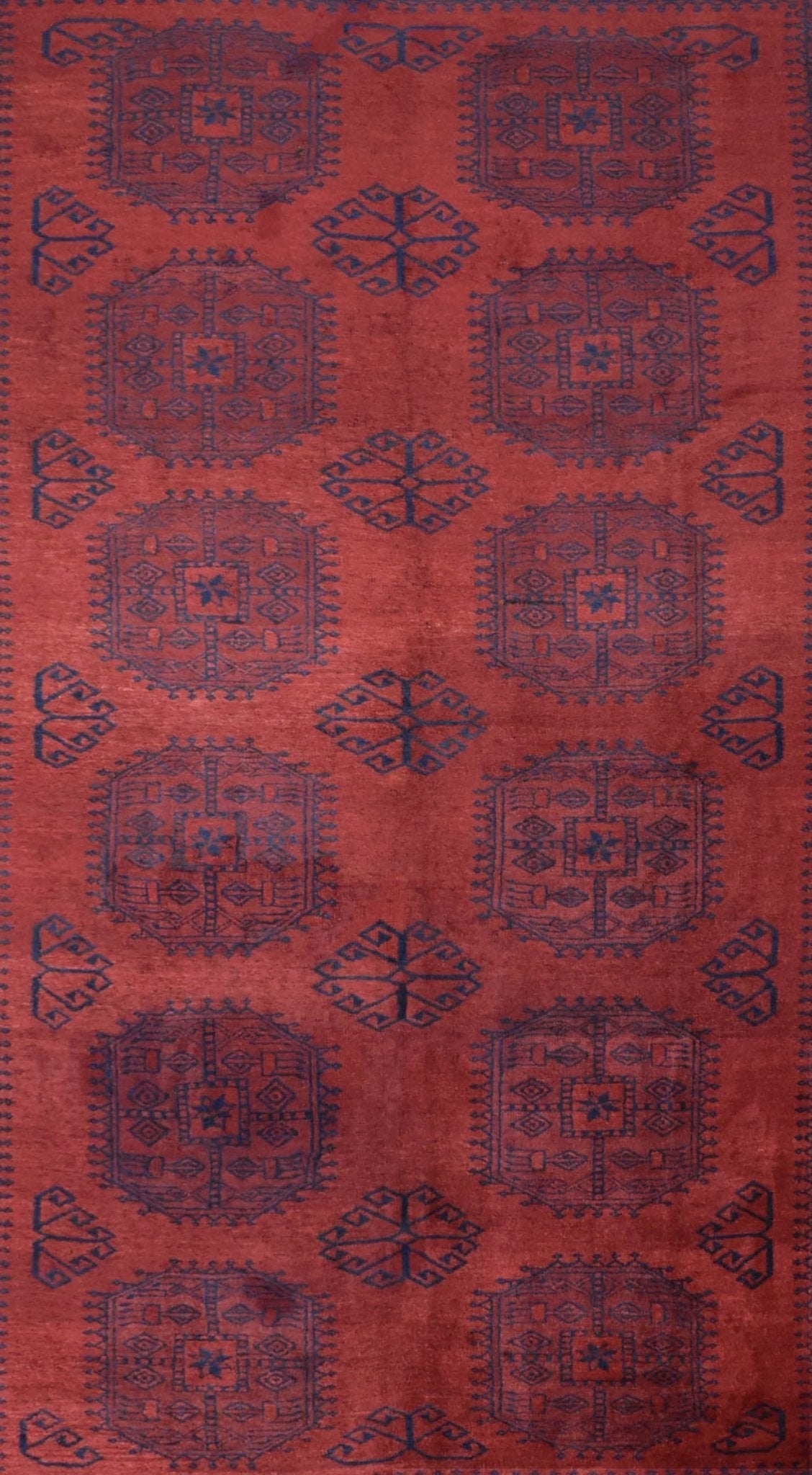 A vintage handmade Afghan Turkmen rug featuring a repeating geometric pattern in blue on a red field.