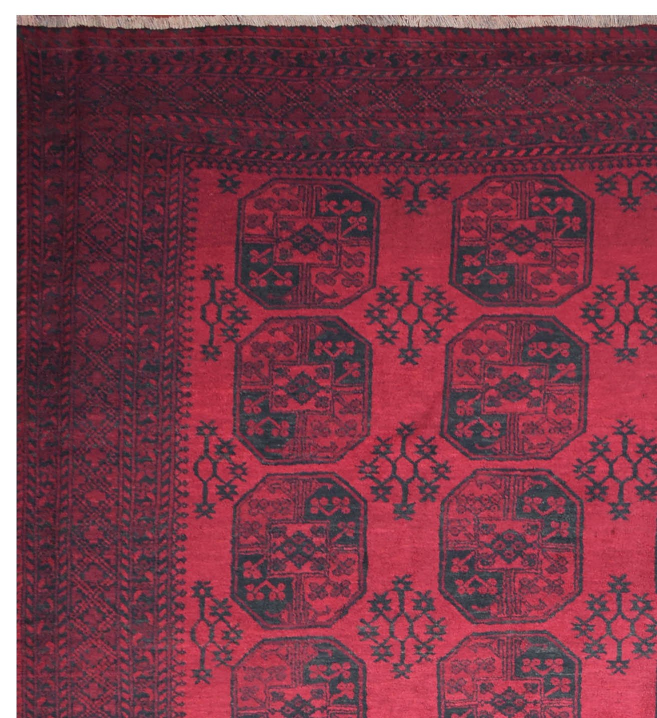 A vintage Afghan Turkmen rug featuring a deep red field with repeating dark geometric octagons.