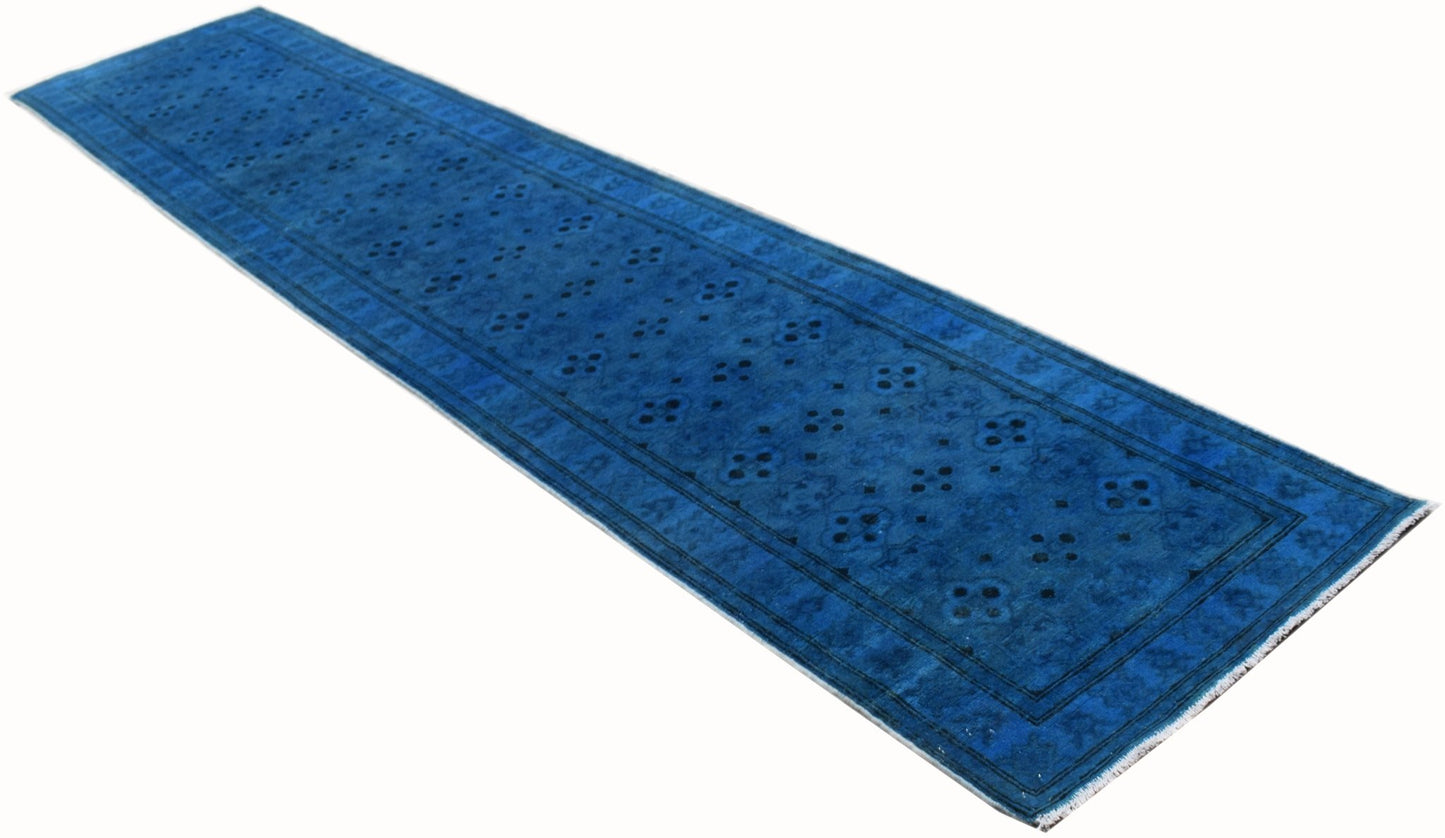 A long, handmade Afghan Chobi runner rug in a vibrant, overdyed blue with a repeating floral pattern.