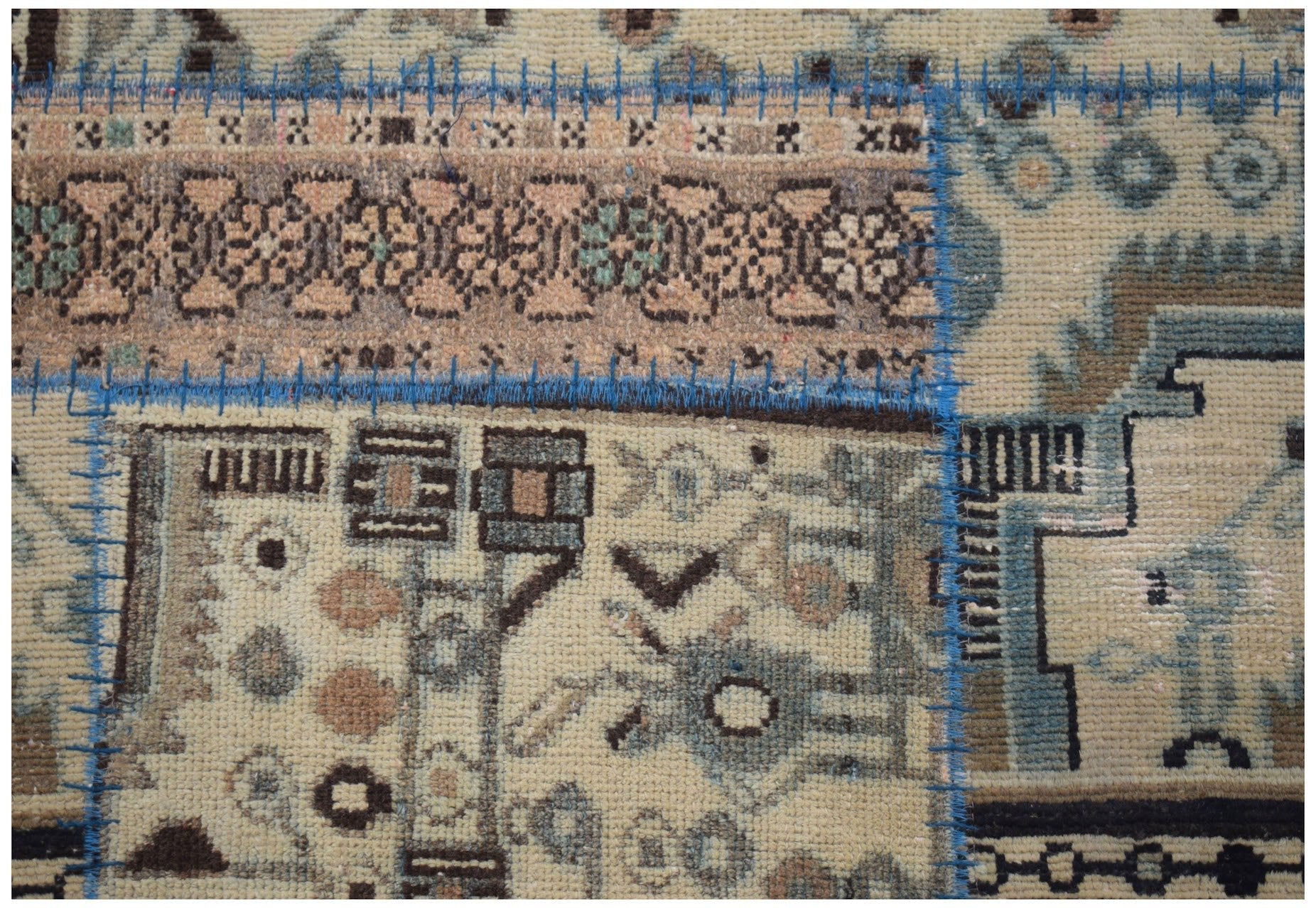 A handmade wool patchwork runner featuring various vintage rug patterns joined by blue stitching.