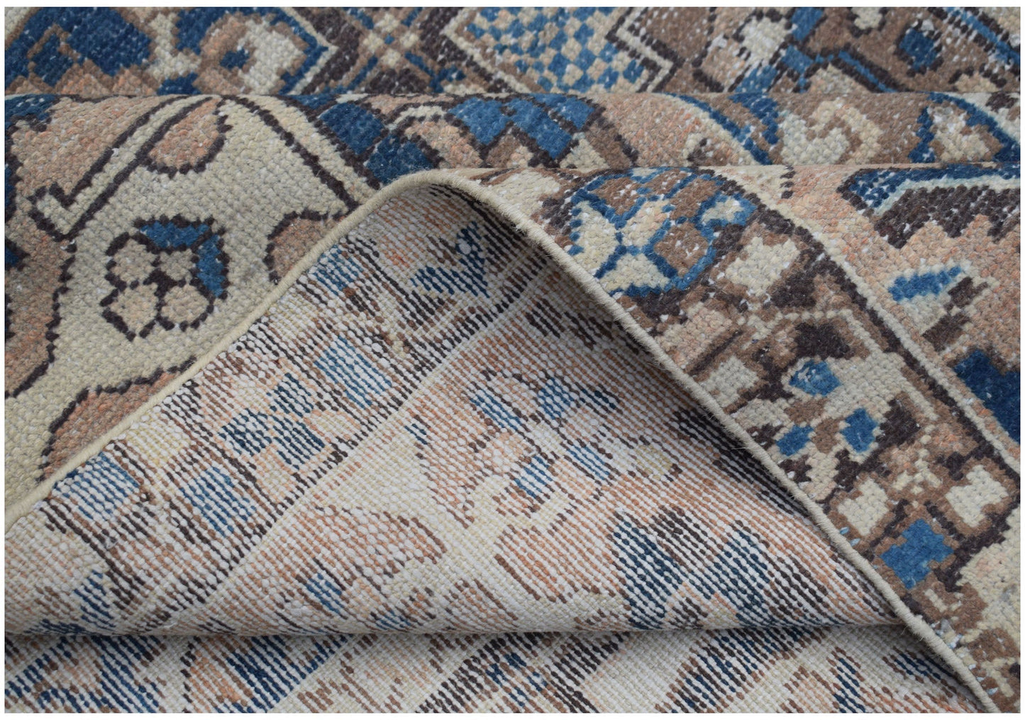 A folded corner of a handmade Persian Bakhtiari rug featuring a geometric pattern in blue and tan.