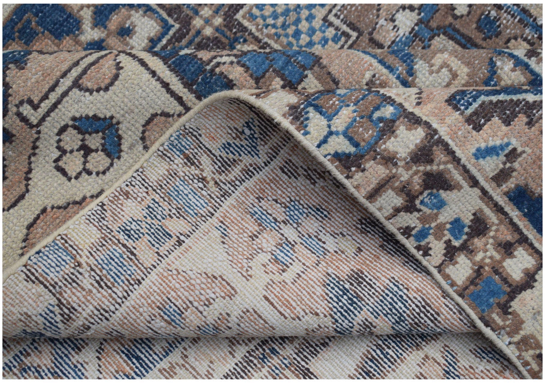 A folded corner of a handmade Persian Bakhtiari rug featuring a geometric pattern in blue and tan.