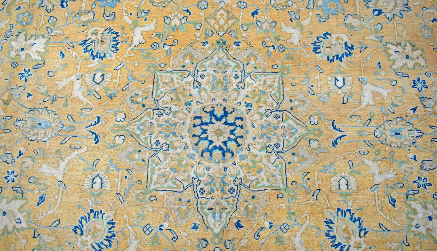 A vintage Persian Kashan rug featuring an intricate floral medallion in blue and cream on gold.