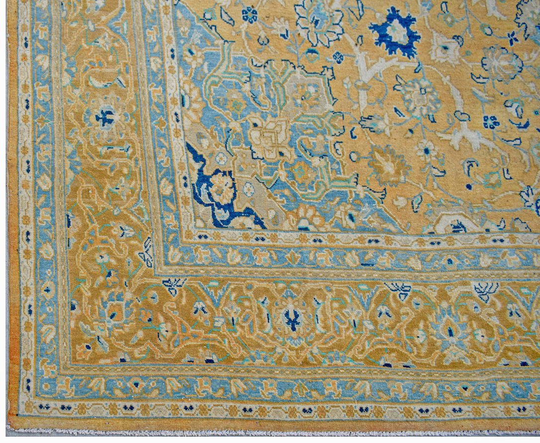 A vintage Persian Kashan rug featuring intricate floral patterns in shades of gold and blue.