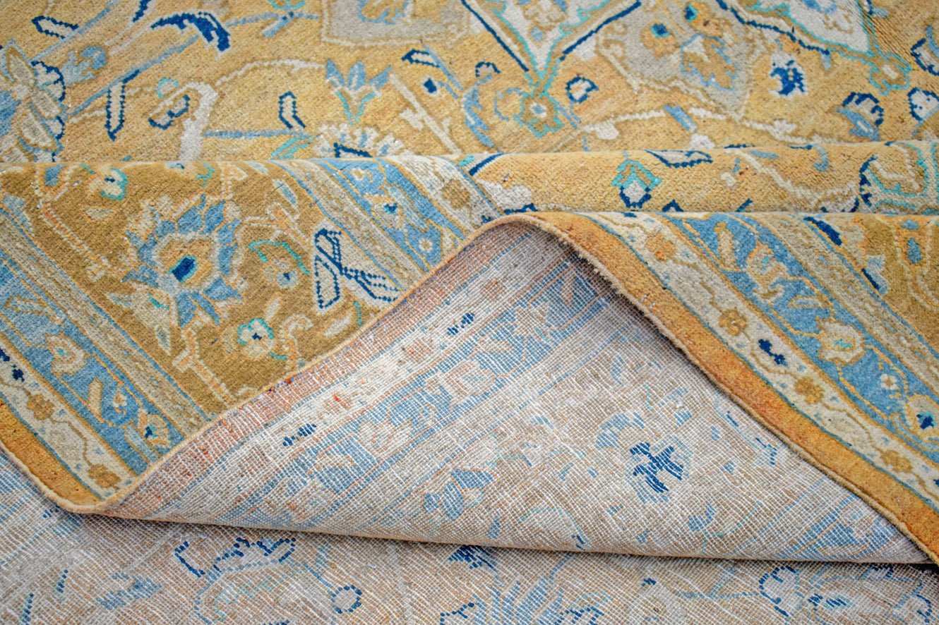 A vintage Persian Kashan rug with a gold and blue floral medallion pattern folded to show the back.