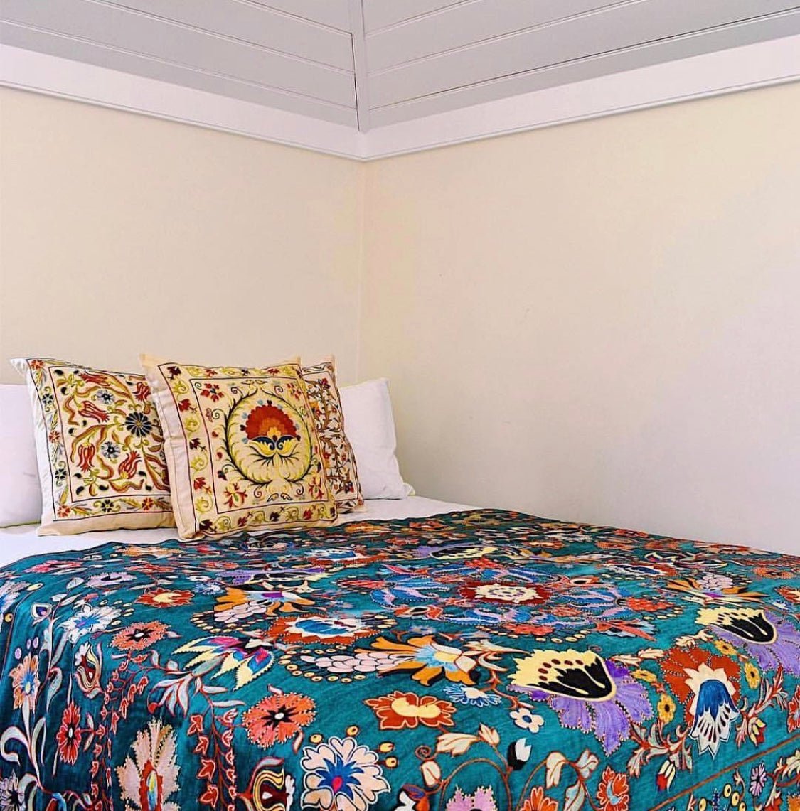 A handmade silk Uzbek suzani with vibrant floral embroidery draped over a bed.
