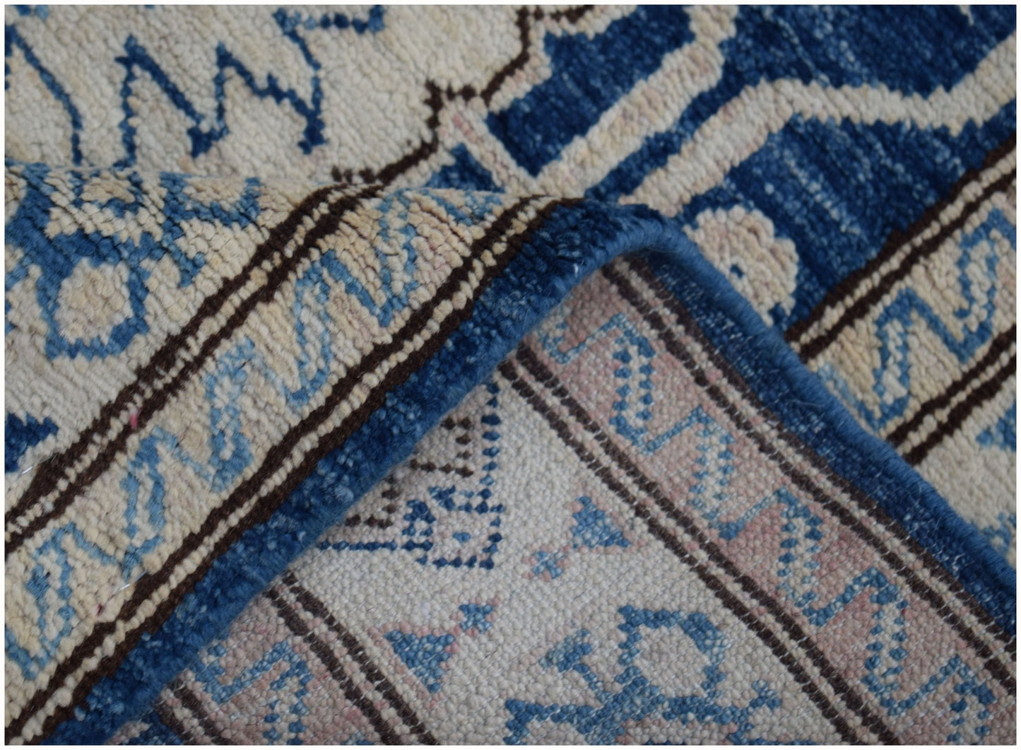 A close-up of a handmade Afghan Super Kazakh runner featuring intricate blue and beige patterns.