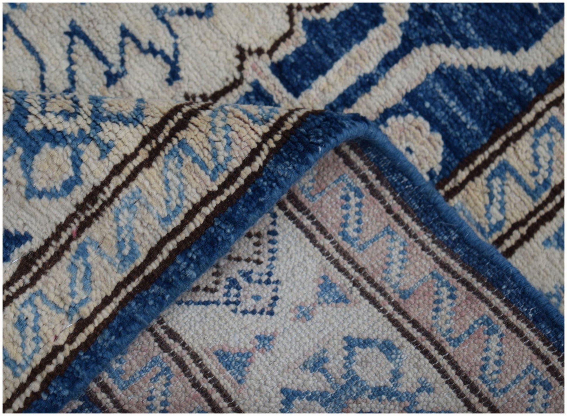 A close-up of a handmade Afghan Super Kazakh runner featuring intricate blue and beige patterns.