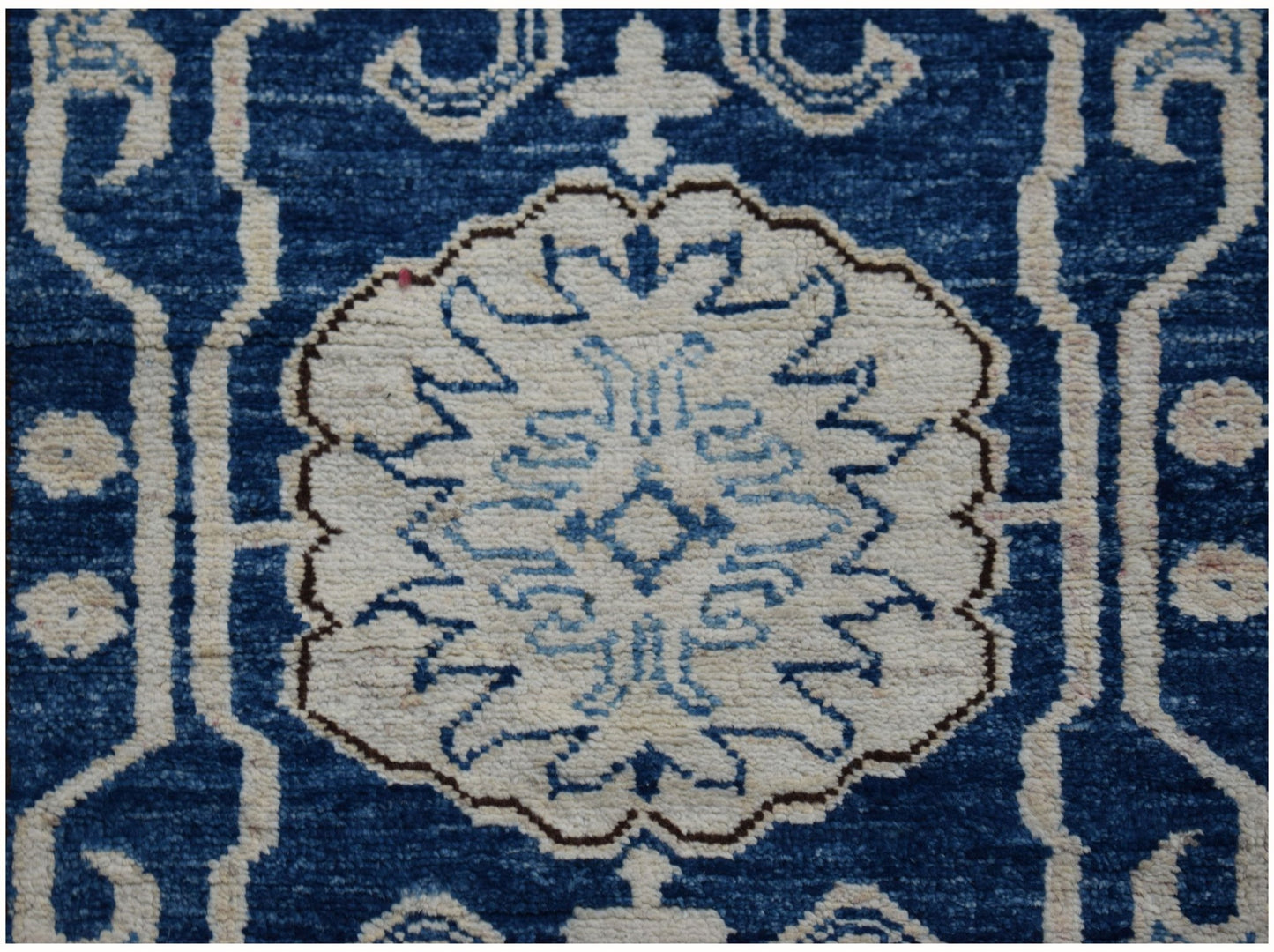 An Afghan Super Kazakh runner rug featuring a central white floral medallion on a blue background.