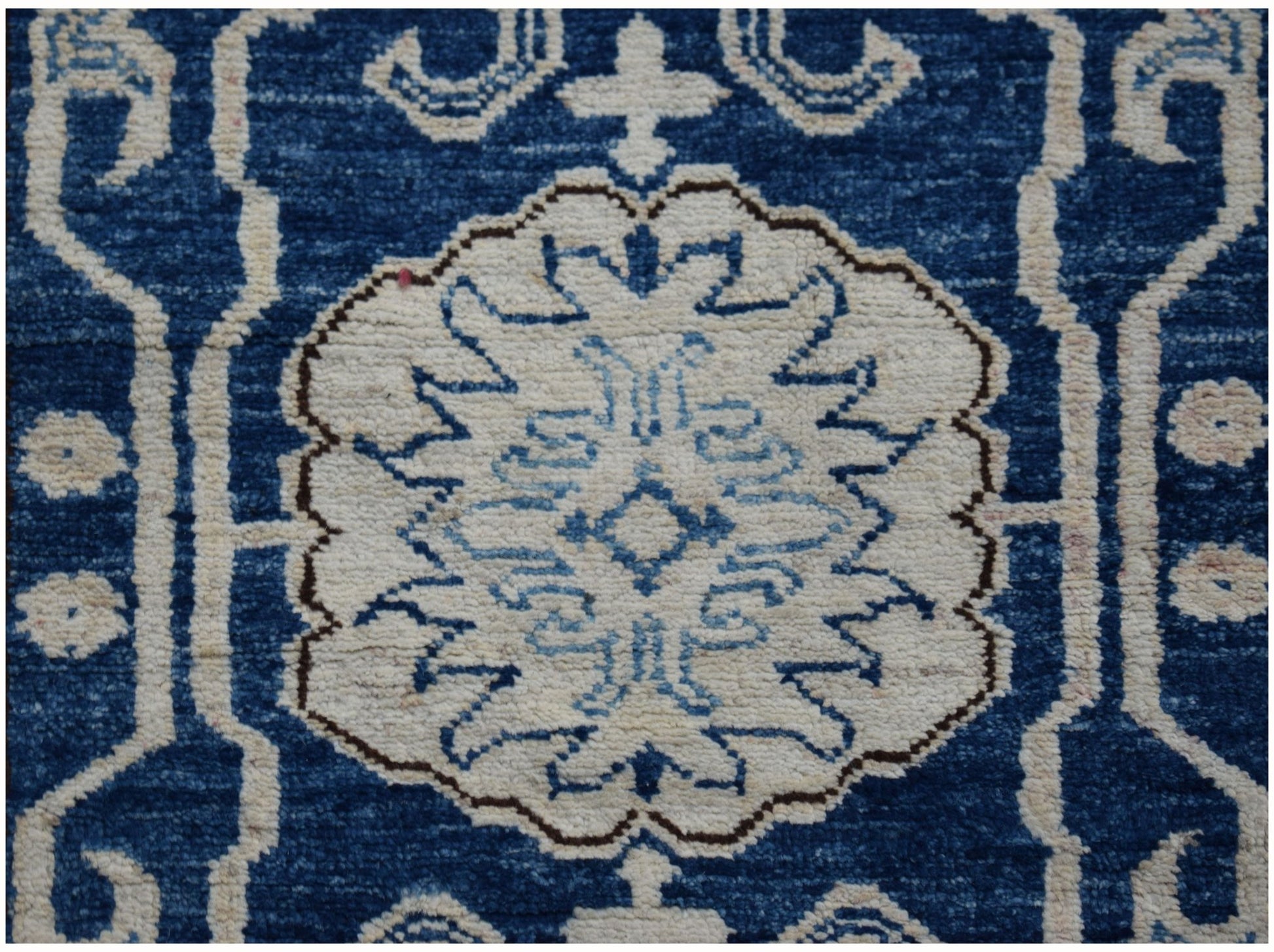 An Afghan Super Kazakh runner rug featuring a central white floral medallion on a blue background.