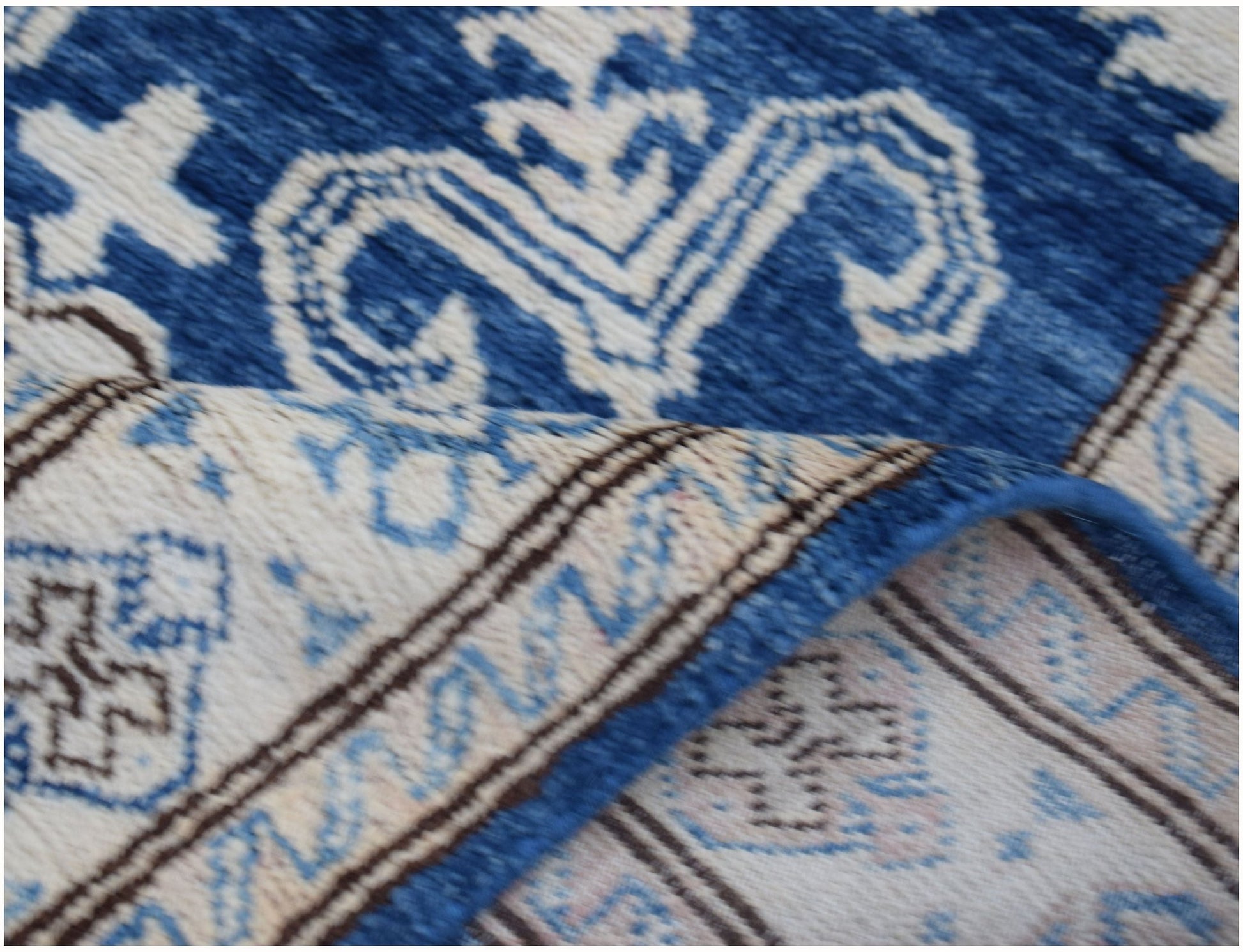 A close-up of a handmade Afghan Super Kazakh runner featuring a blue and beige geometric pattern.