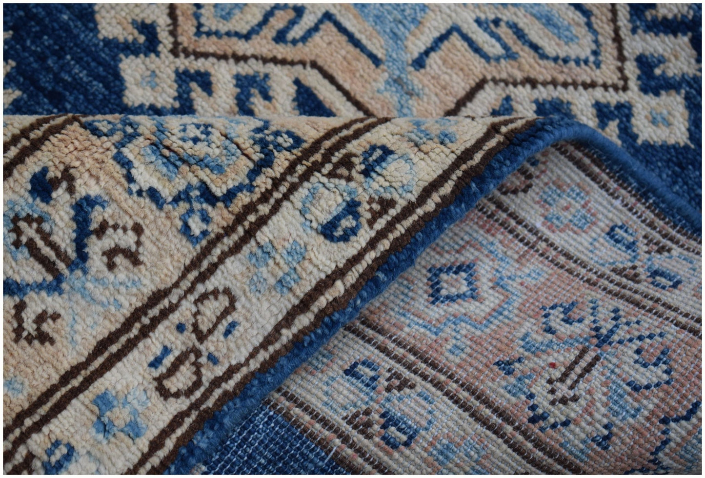 A folded Afghan Super Kazakh runner rug featuring a geometric pattern in blue, beige, and grey.