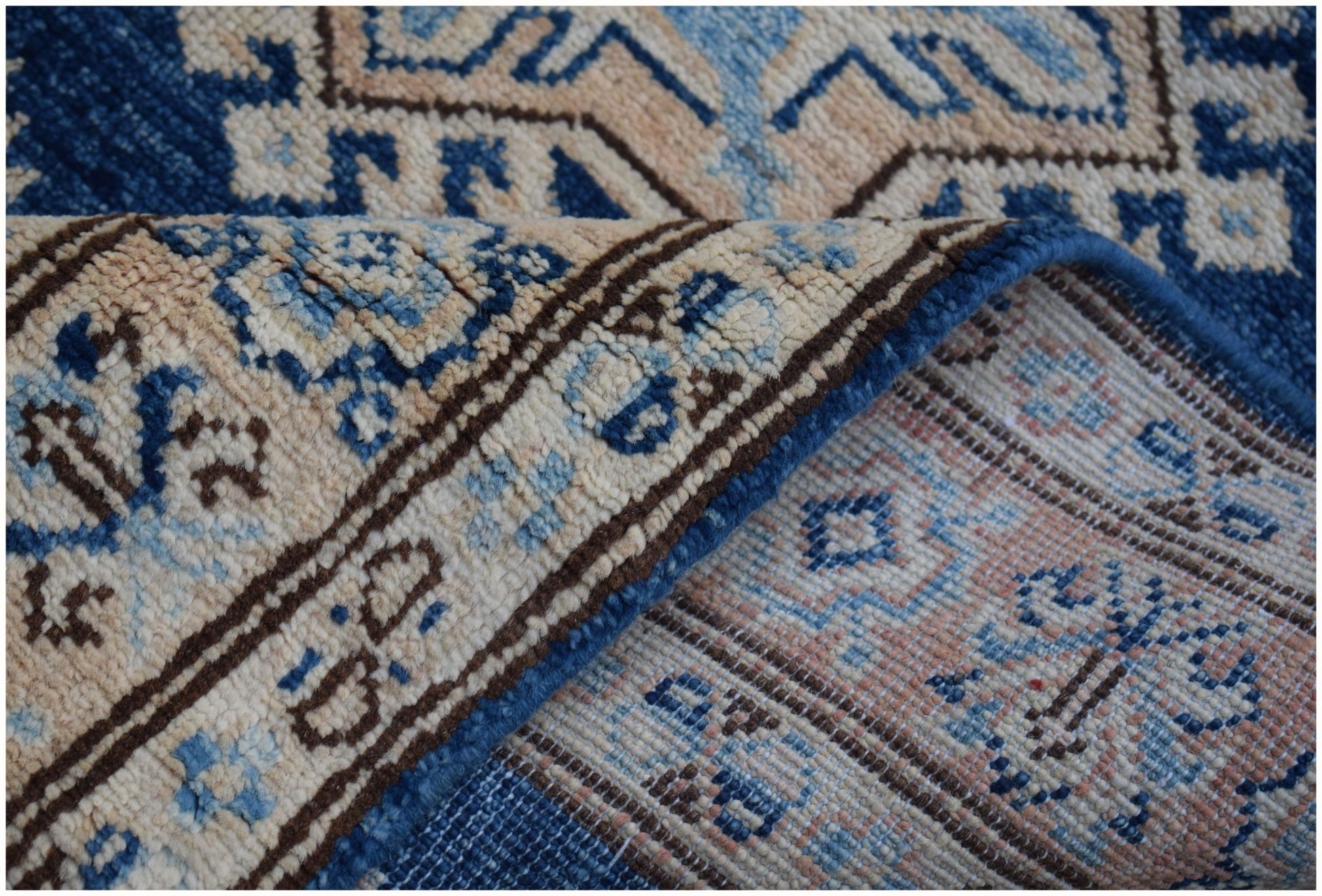 A folded Afghan Super Kazakh runner rug featuring a geometric pattern in blue, beige, and grey.