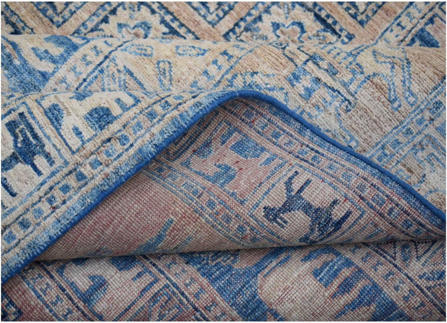A handmade Afghan Chobi rug featuring a blue and beige geometric pattern with a folded corner.