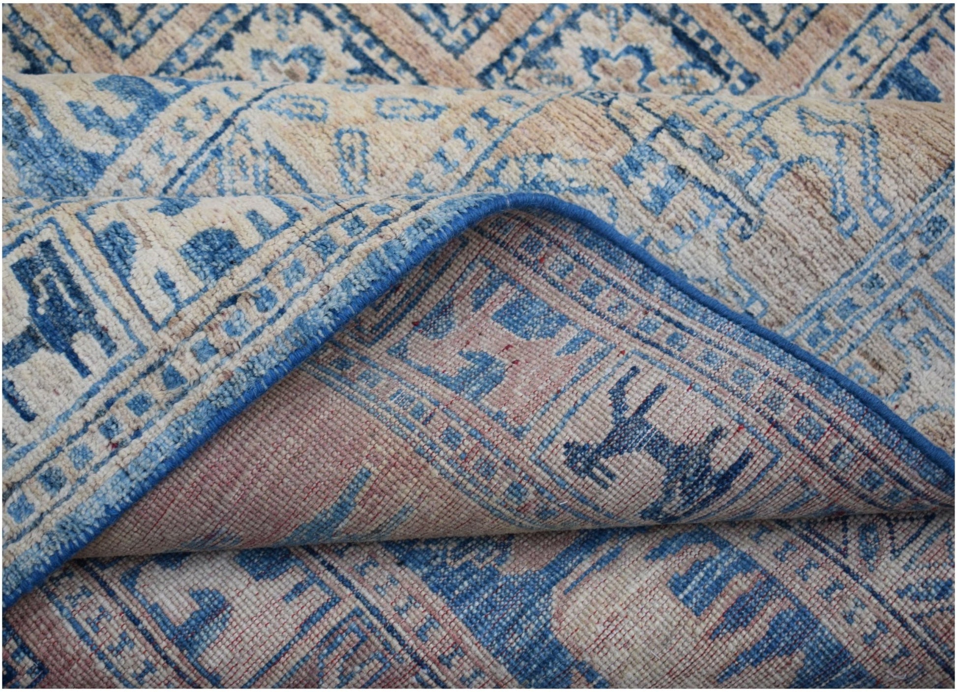 A handmade Afghan Chobi rug featuring a blue and beige geometric pattern with a folded corner.