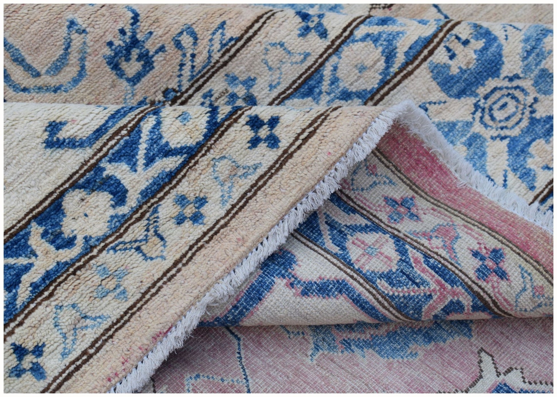 A folded Afghan Super Kazakh rug featuring a beige, blue, and pink floral pattern.