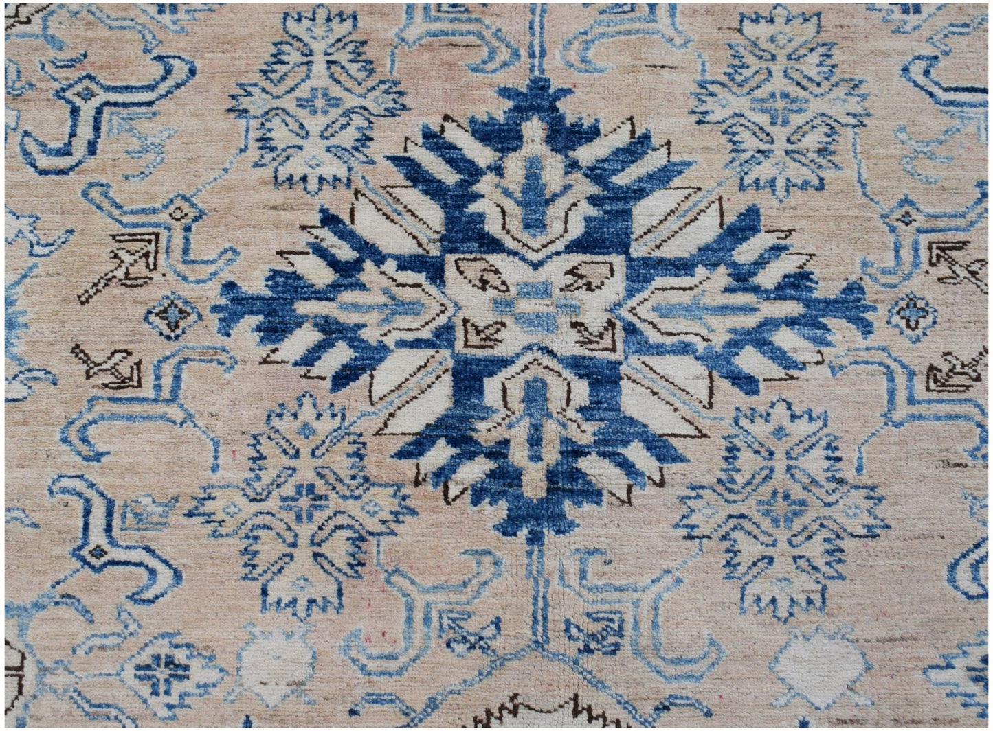An Afghan Super Kazakh rug featuring a central blue geometric medallion on a beige wool field.