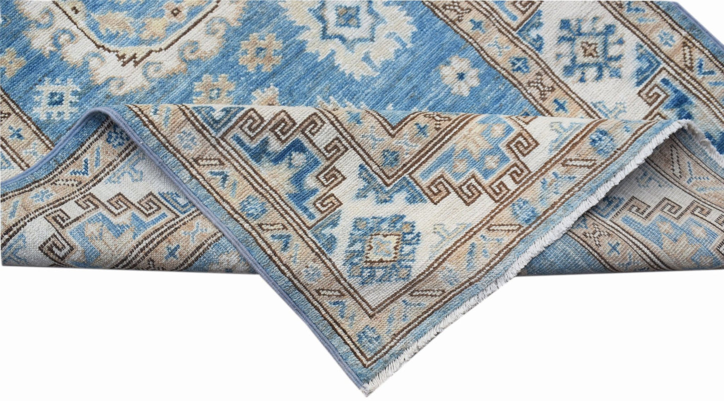 A folded Afghan Super Kazakh runner featuring traditional blue and beige geometric patterns.